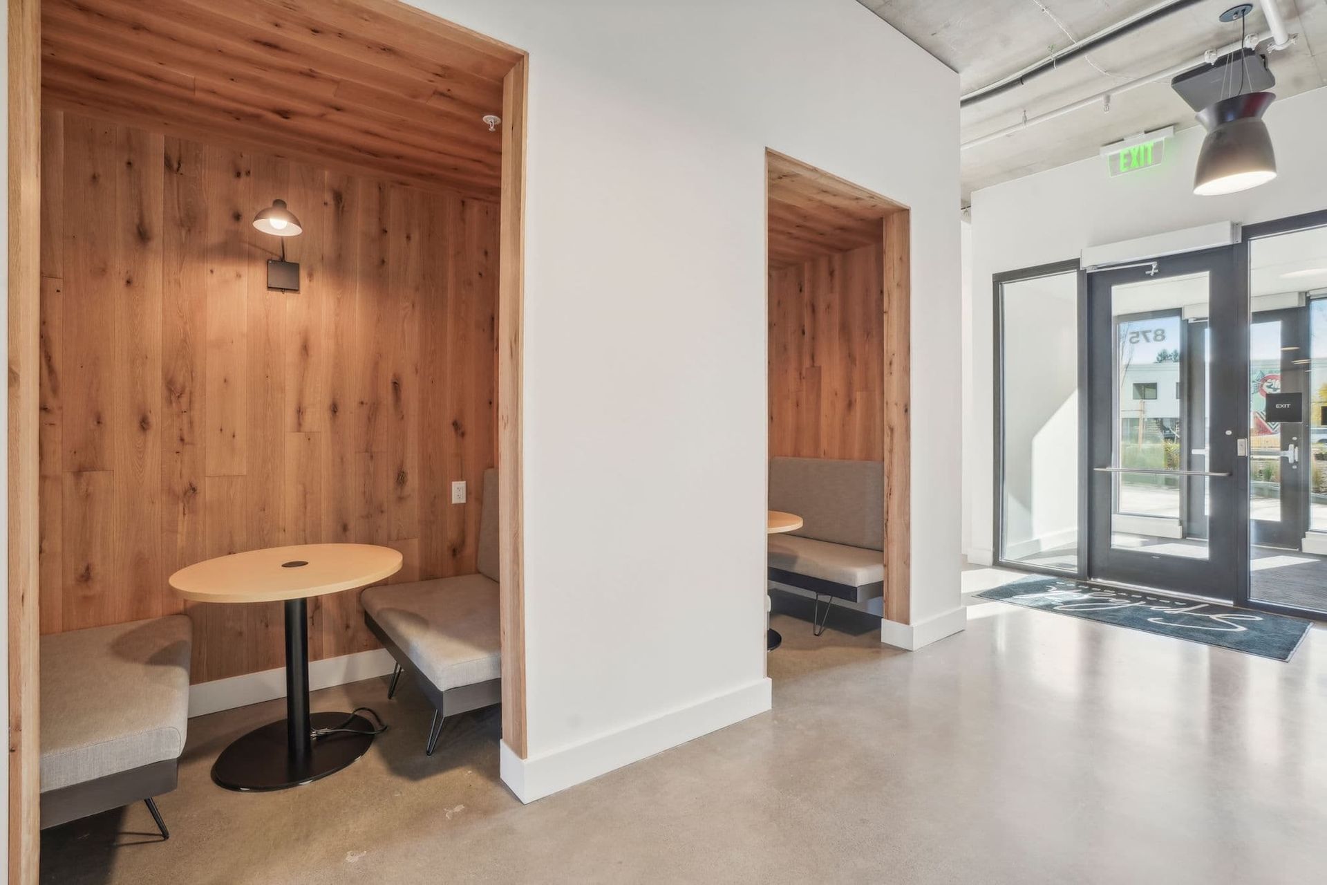 Modern office lounge with wood-paneled seating nook, round table, and glass entrance doors