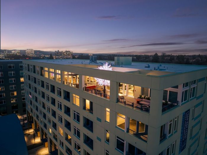 Rooftop restaurant at dusk in a modern apartment building, with glowing windows and city skyline in the background