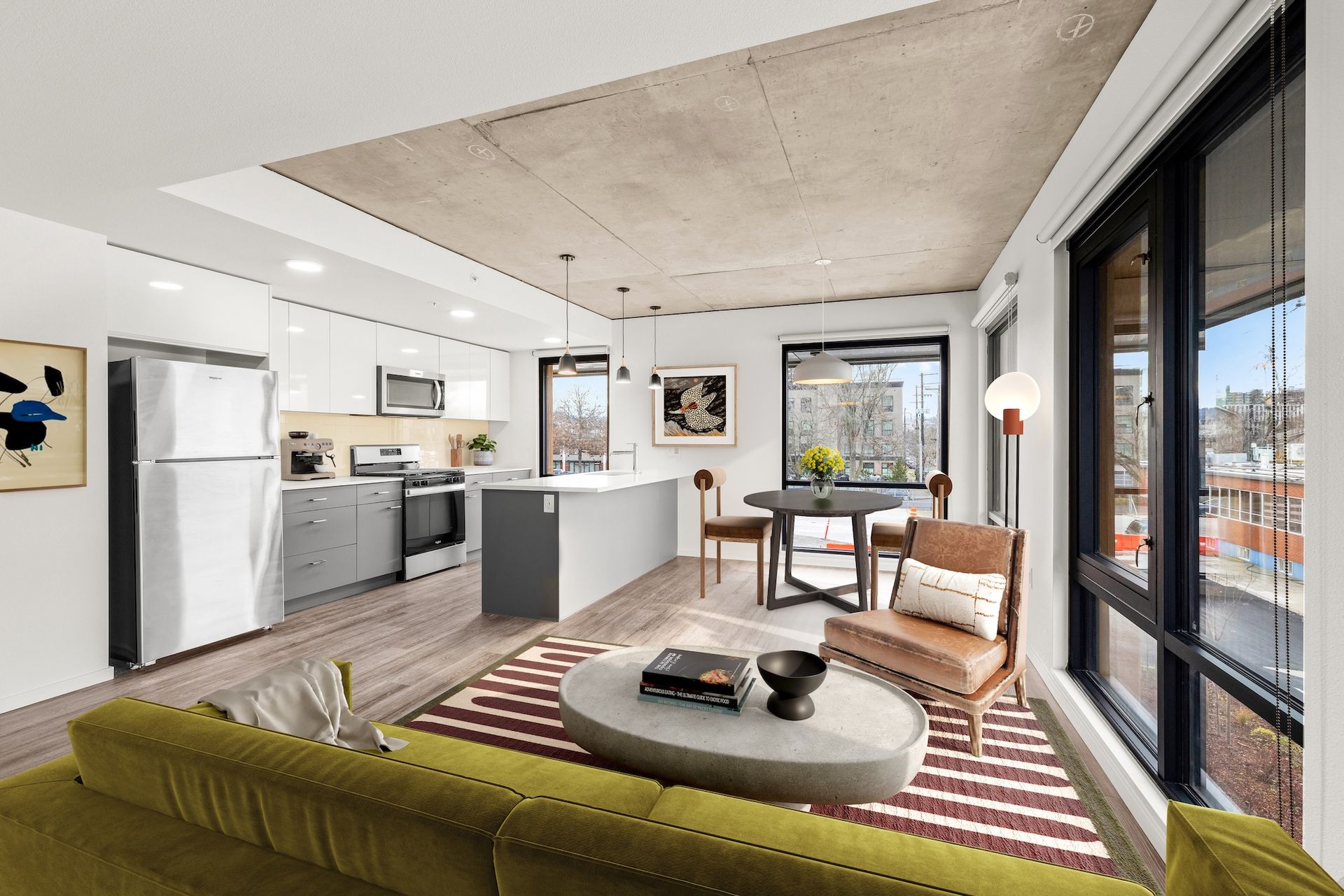 Bright modern loft living room with kitchen, large windows, striped rug, and green sofa.