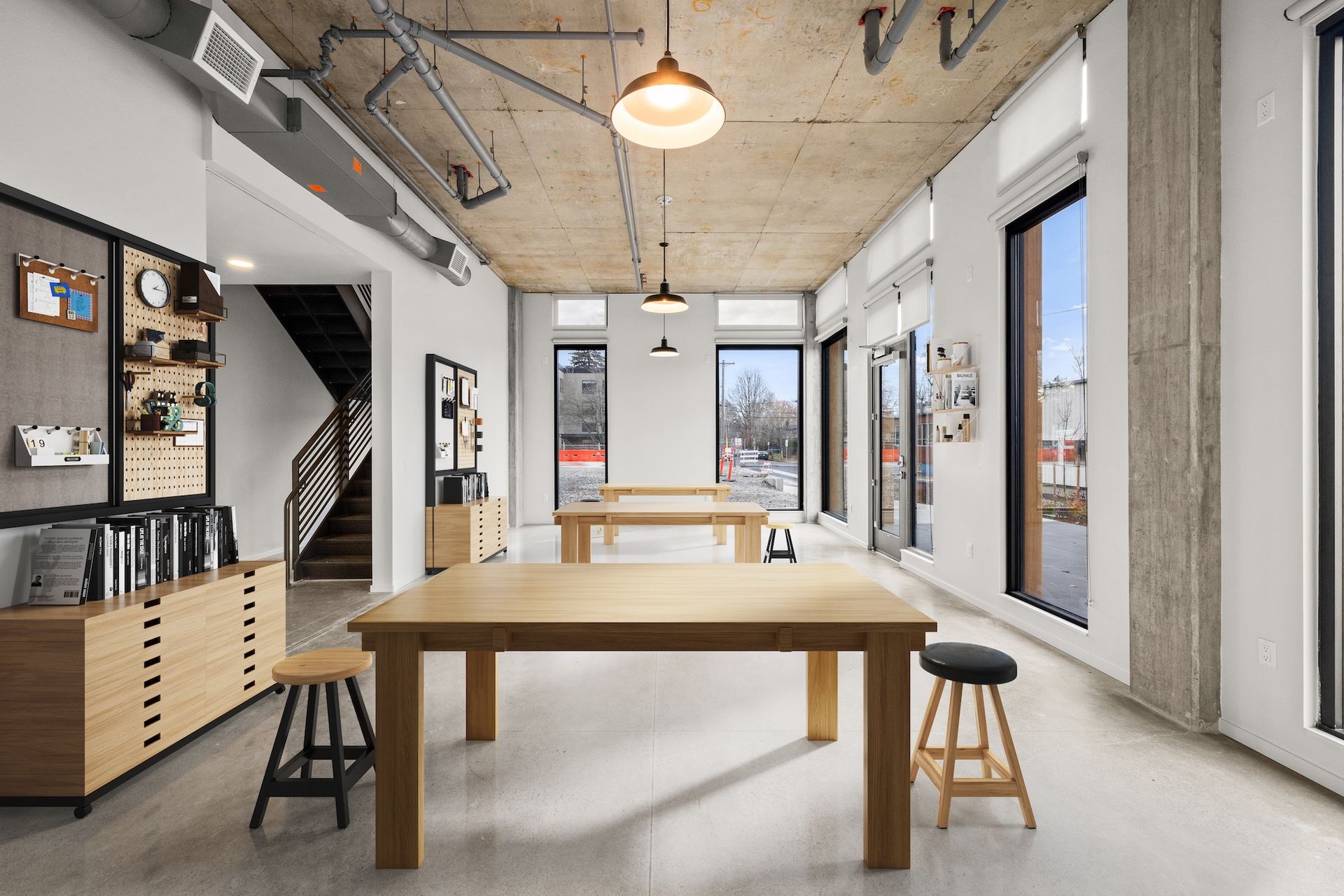 Bright modern dining room with a wooden table, stools, large windows, and high ceiling