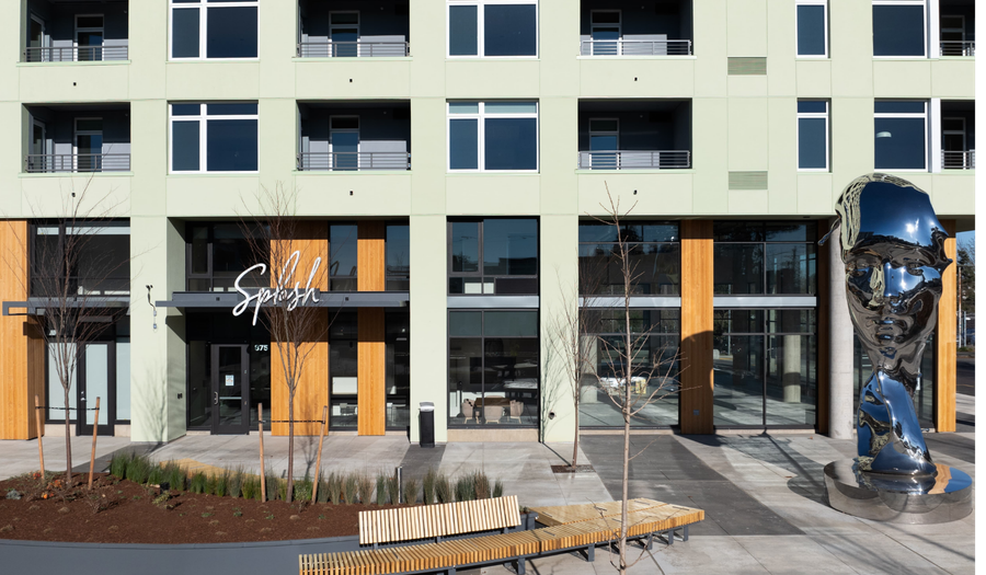 Modern apartment building facade with glass storefronts and a blue reflective sculpture outside.