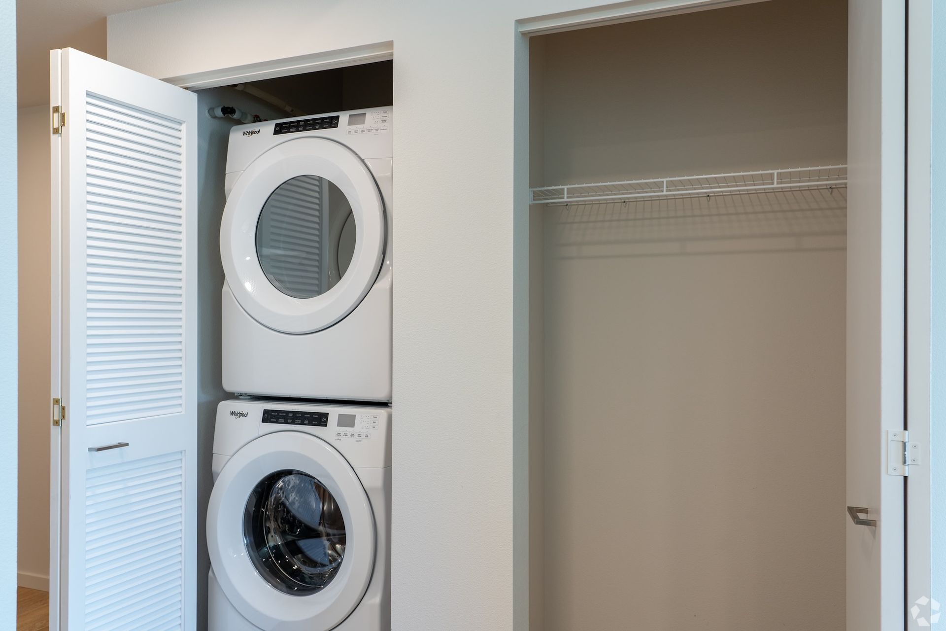 Laundry closet with stacked washer and dryer beside an empty closet with shelves