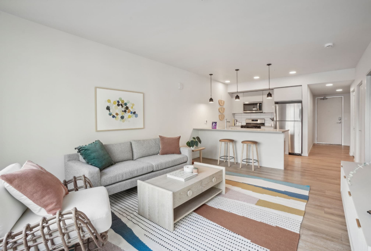 Bright open-plan living room with gray sofa, striped rug, and white kitchen bar stools.