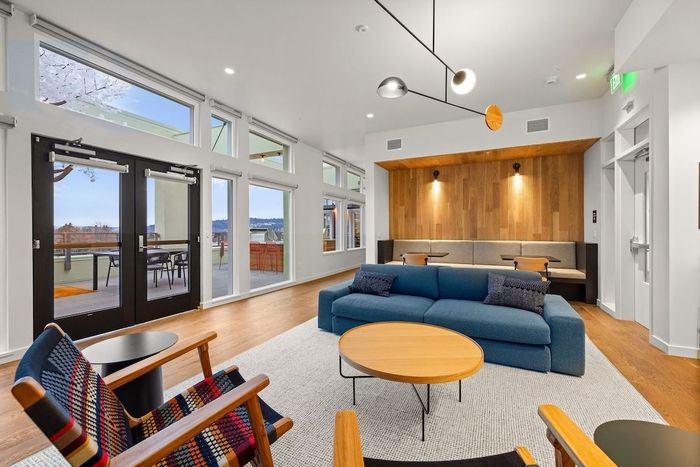 Modern living room with blue sofa, round wood table, large windows, and open kitchen area