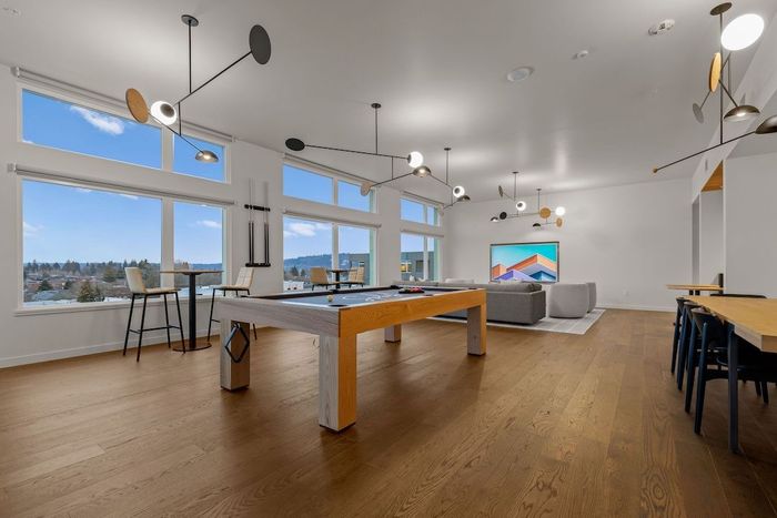 Bright modern game room with a pool table, large windows, wooden floor, and a seating area.
