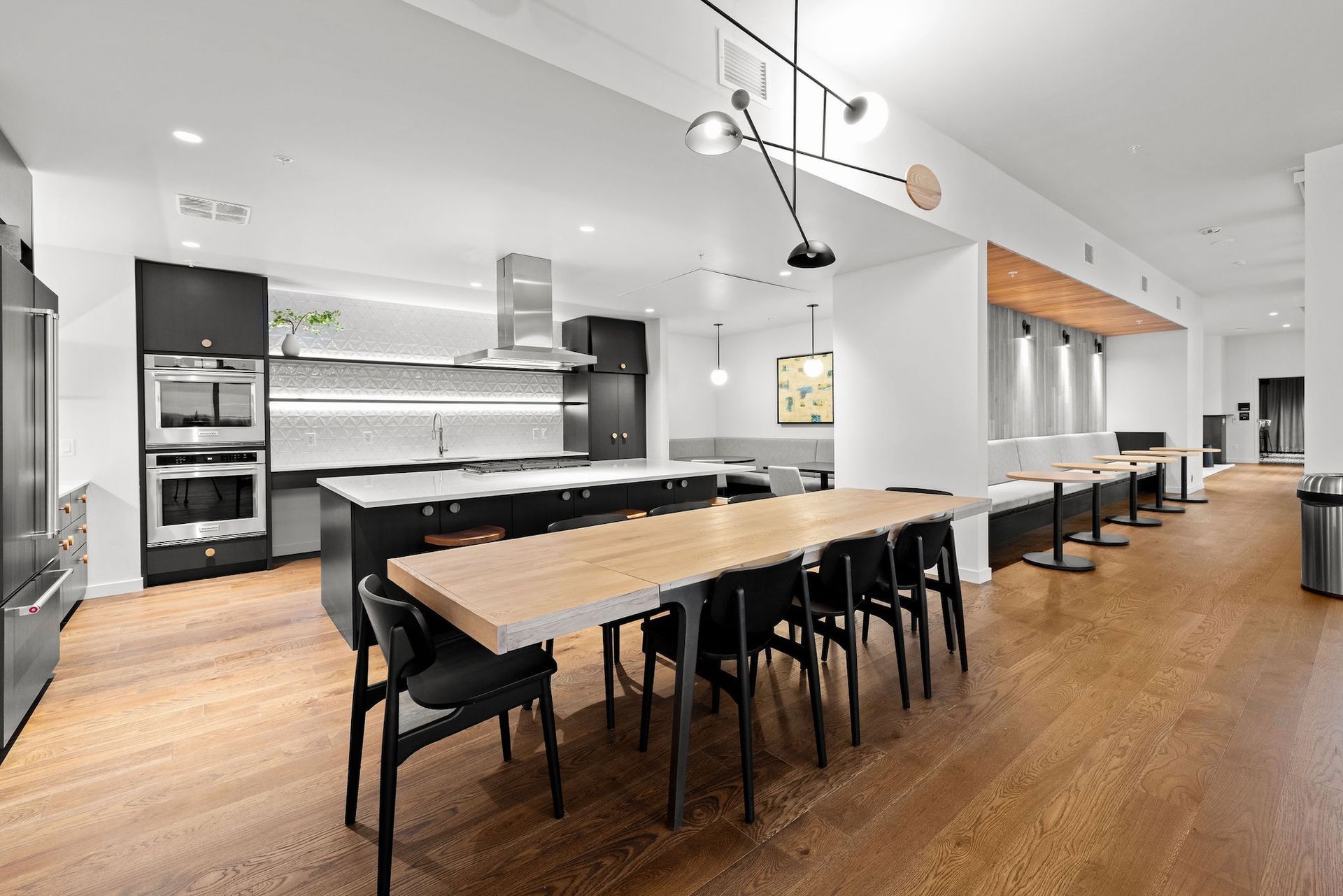 Modern kitchen and dining area with long wooden table, black chairs, and stainless steel appliances