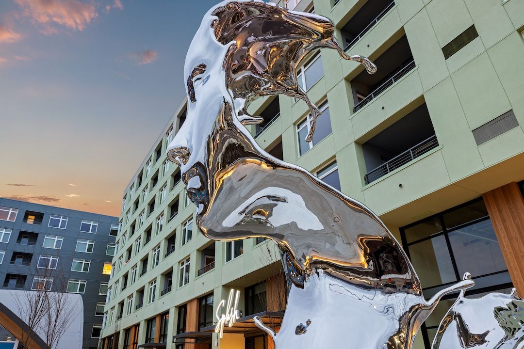 Shiny abstract sculpture before a modern apartment building at sunset