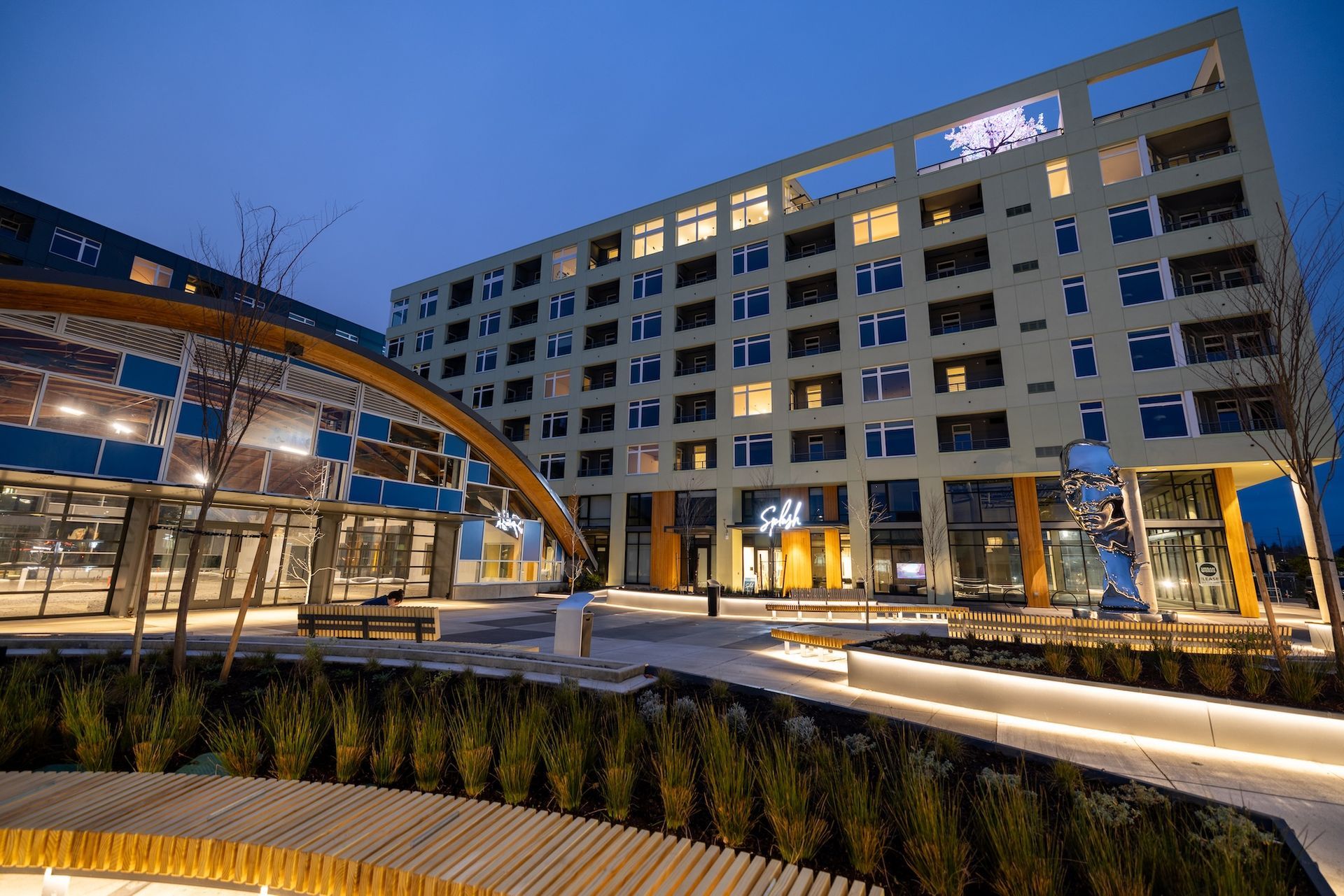 Modern hotel courtyard at dusk with illuminated building, walkway, and landscaped planters