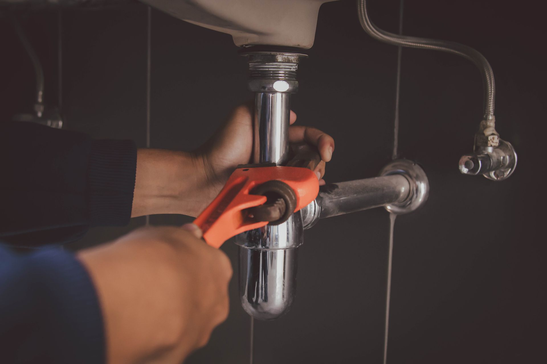 A plumber is fixing a sink pipe with a wrench.