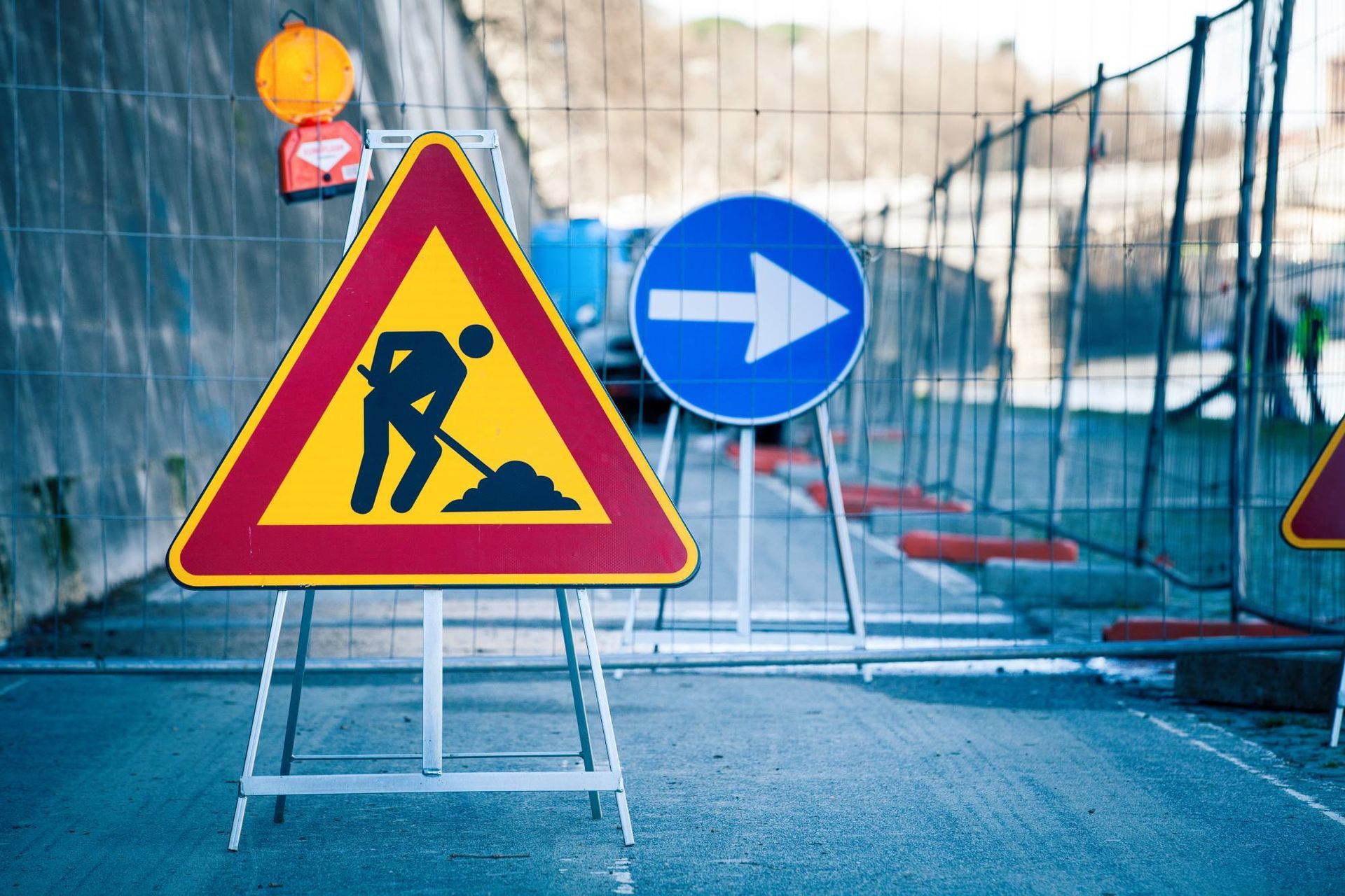 Road work ahead with detour; yellow triangle sign with worker, blue arrow sign; fenced area.