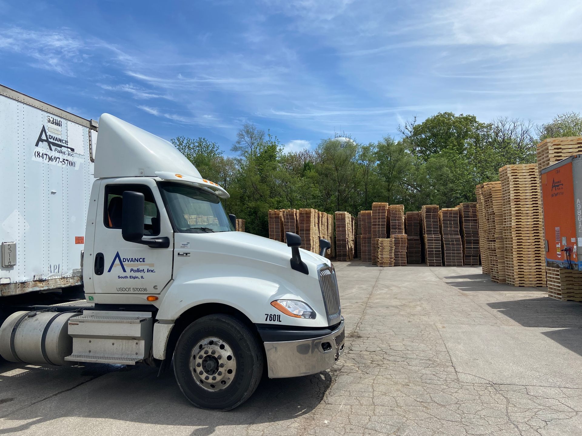 A white semi truck is parked in front of a pile of wooden pallets.
