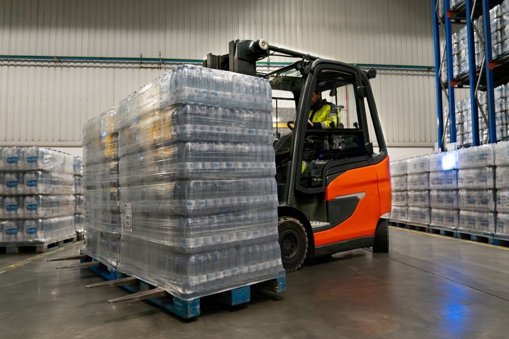A forklift is carrying a pallet of water bottles in a warehouse.