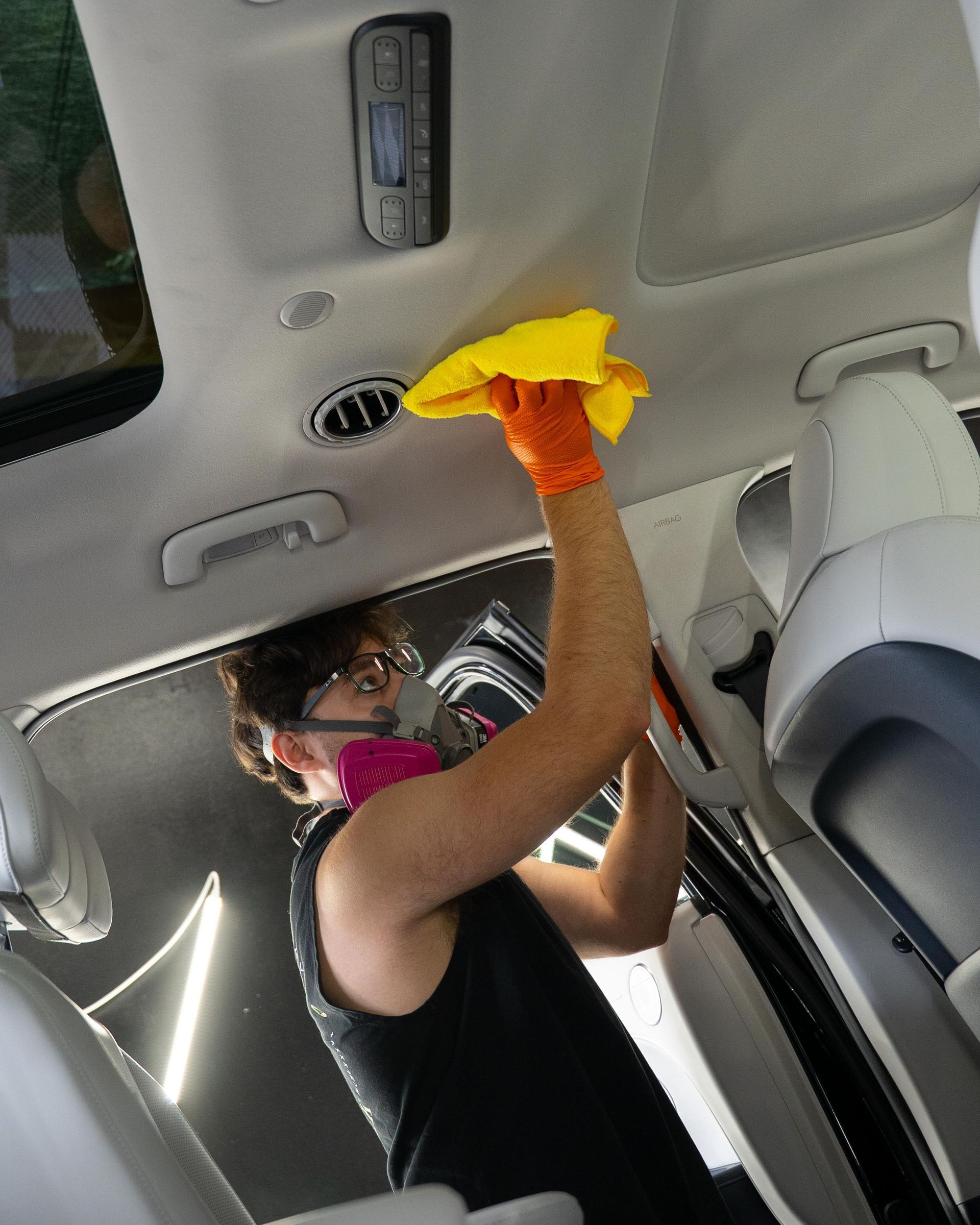 Gloved hand vacuuming dirt from a red car seat with a black hose