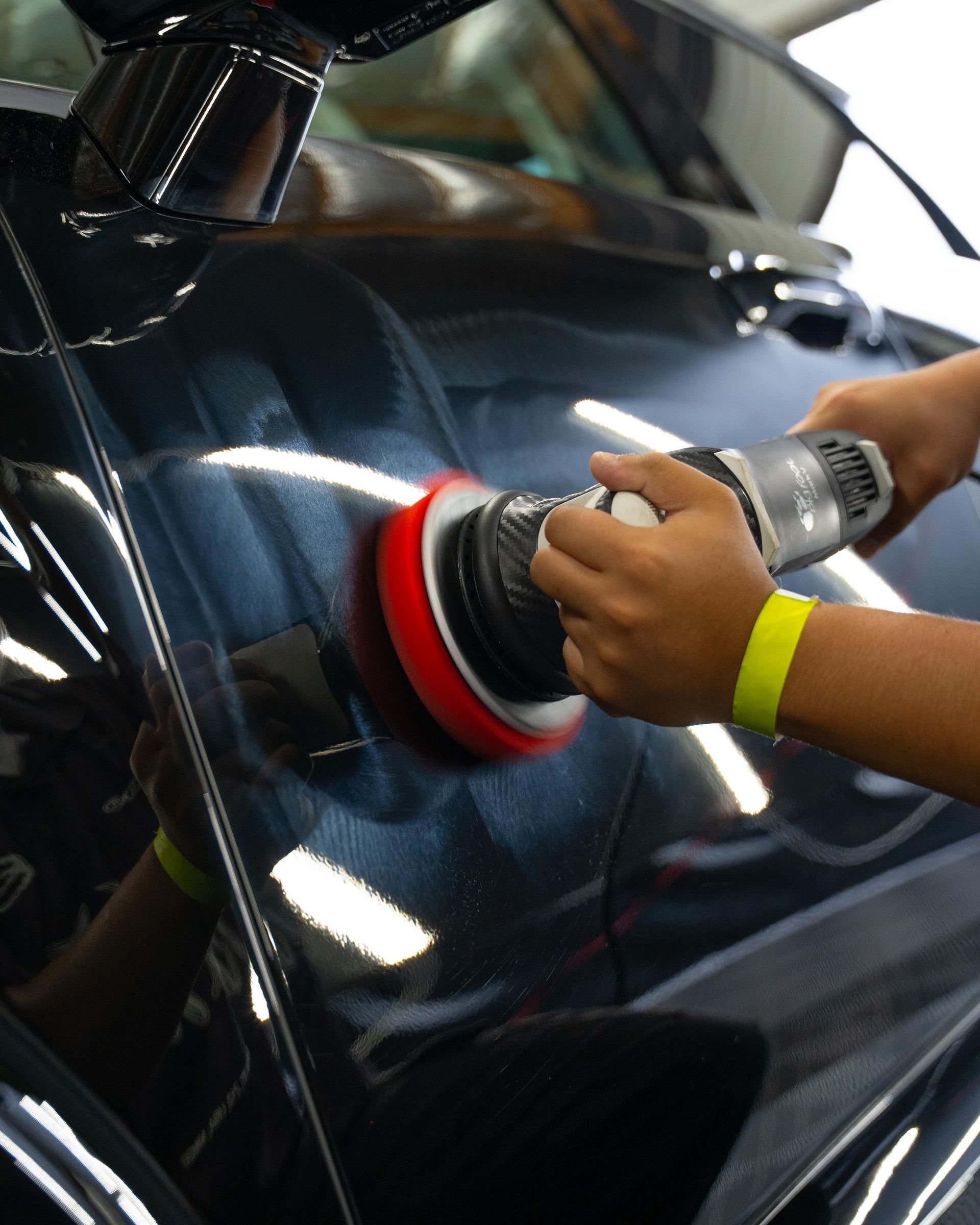 Person using a red and black buffer to polish a black car door
