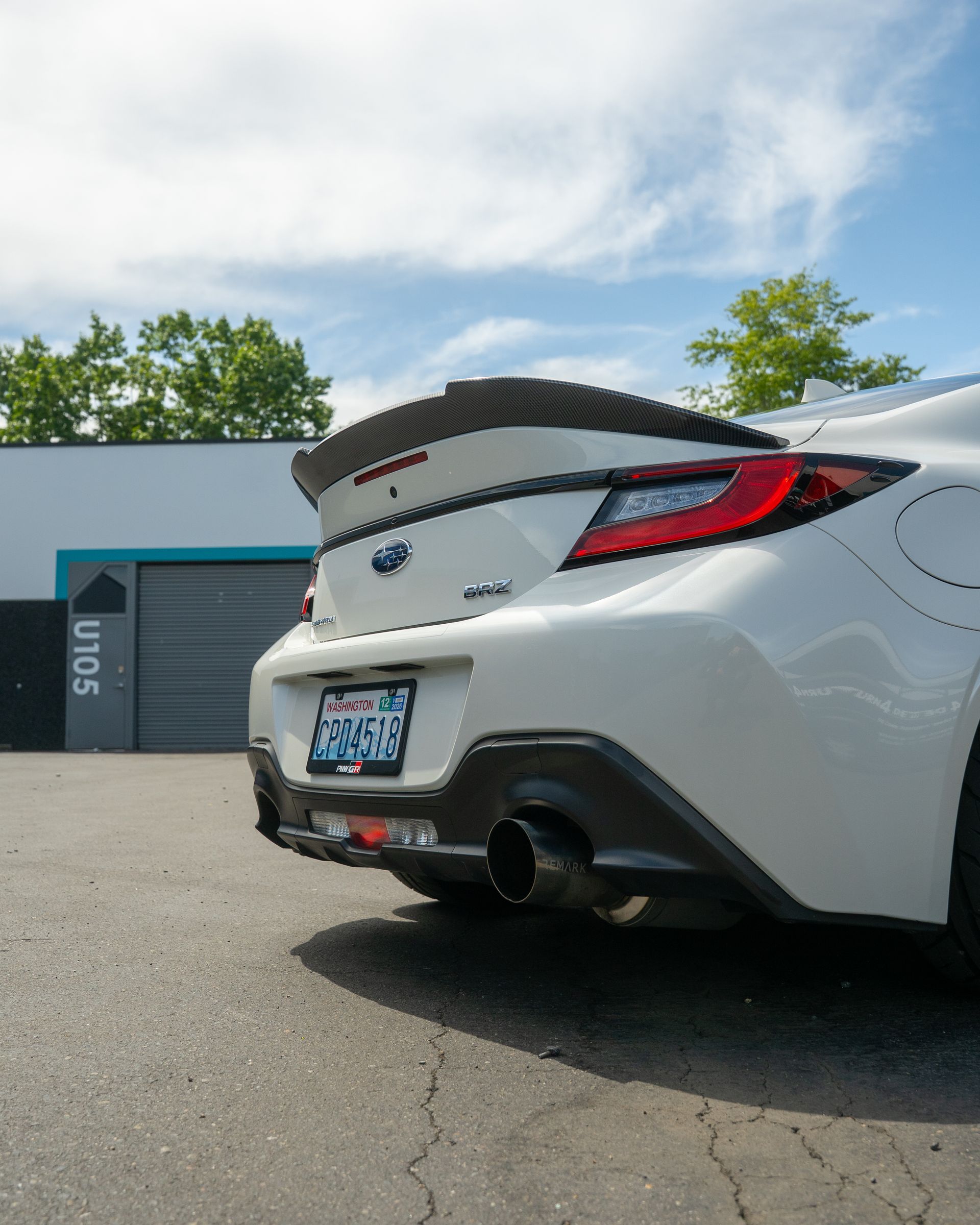 Rear view of a white sports car with a spoiler parked outside a building under a blue sky.