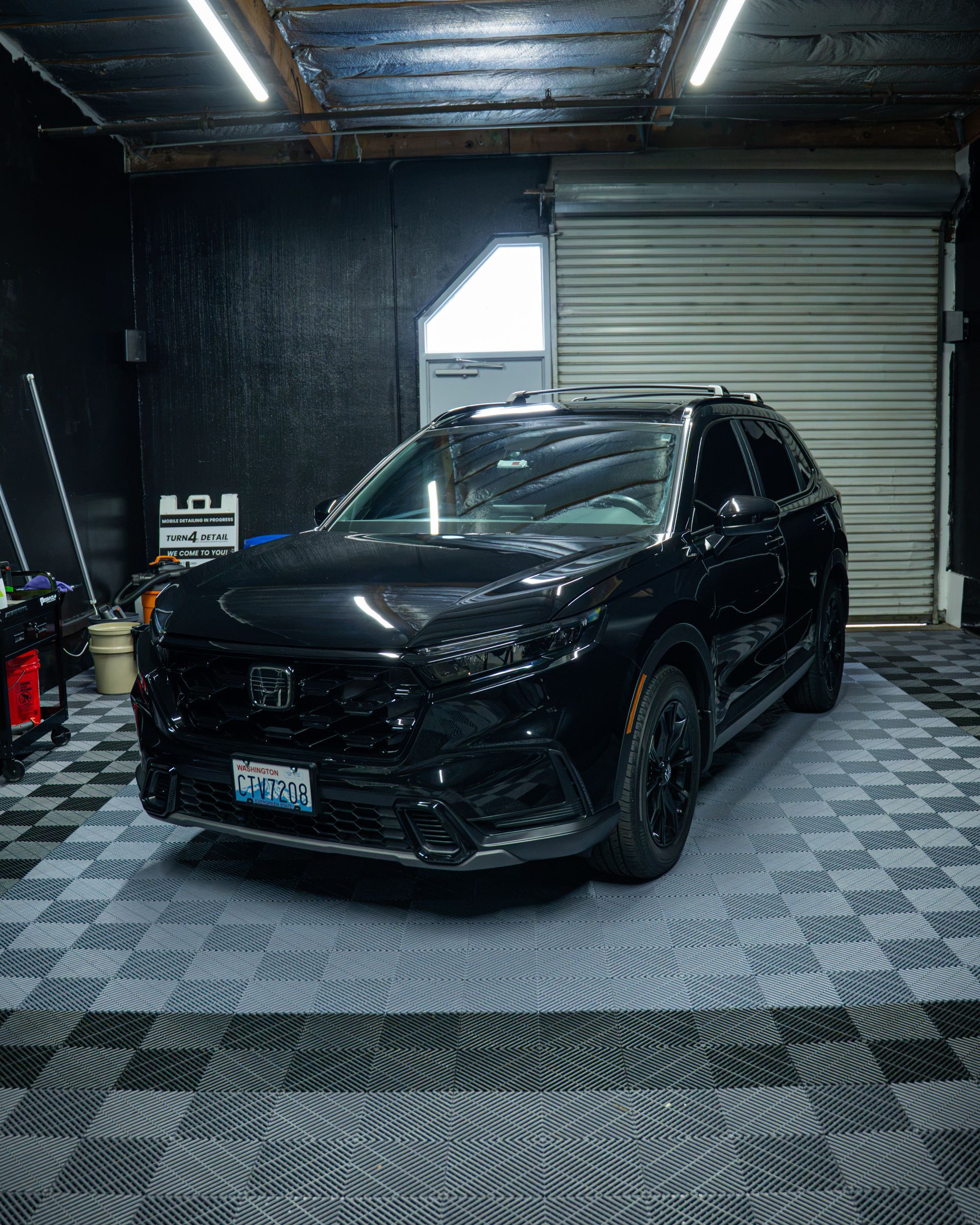 Black SUV parked in a dim garage with a rolled-up metal door and checkered floor tiles.
