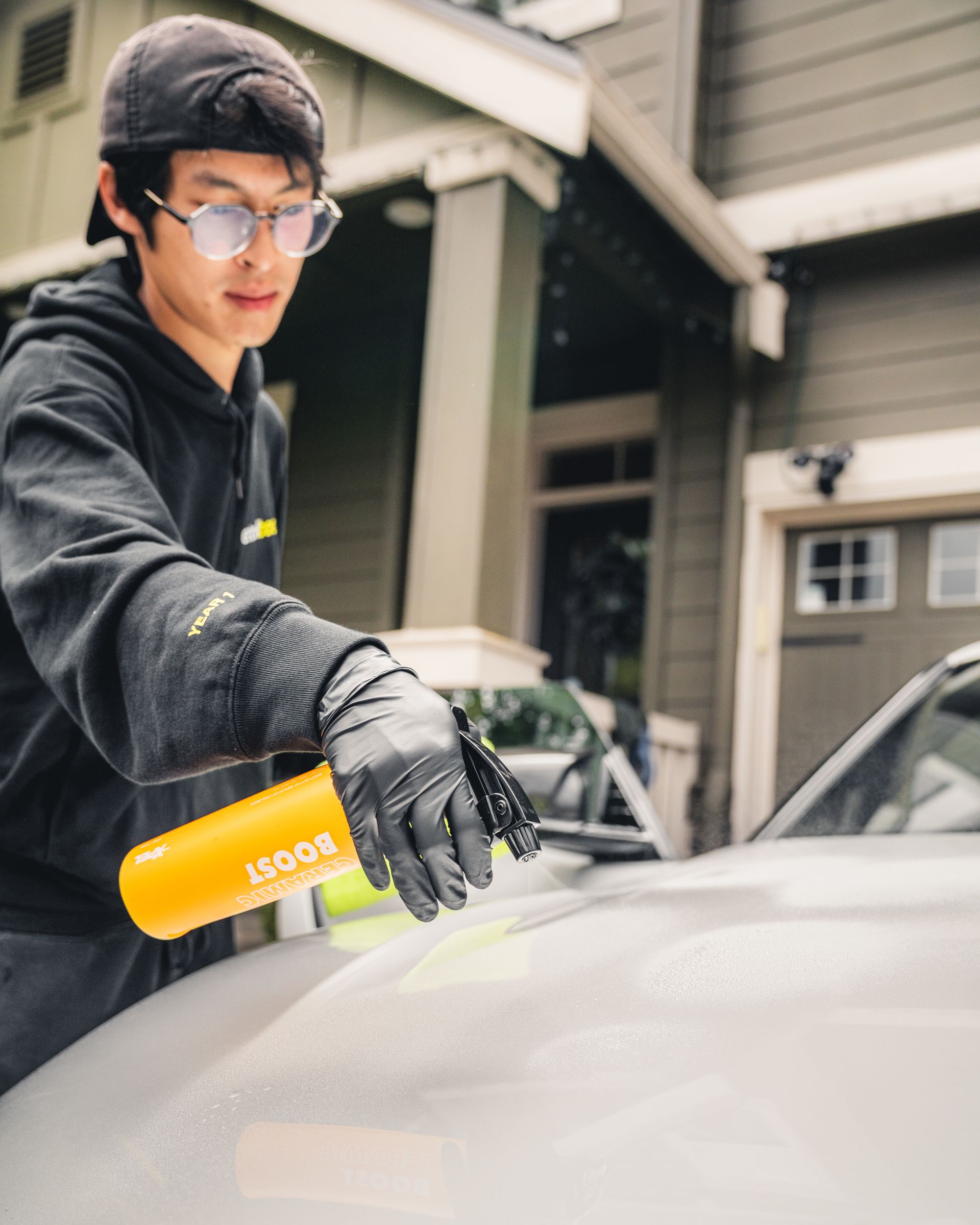 Person using a yellow spray bottle to clean a car hood outdoors