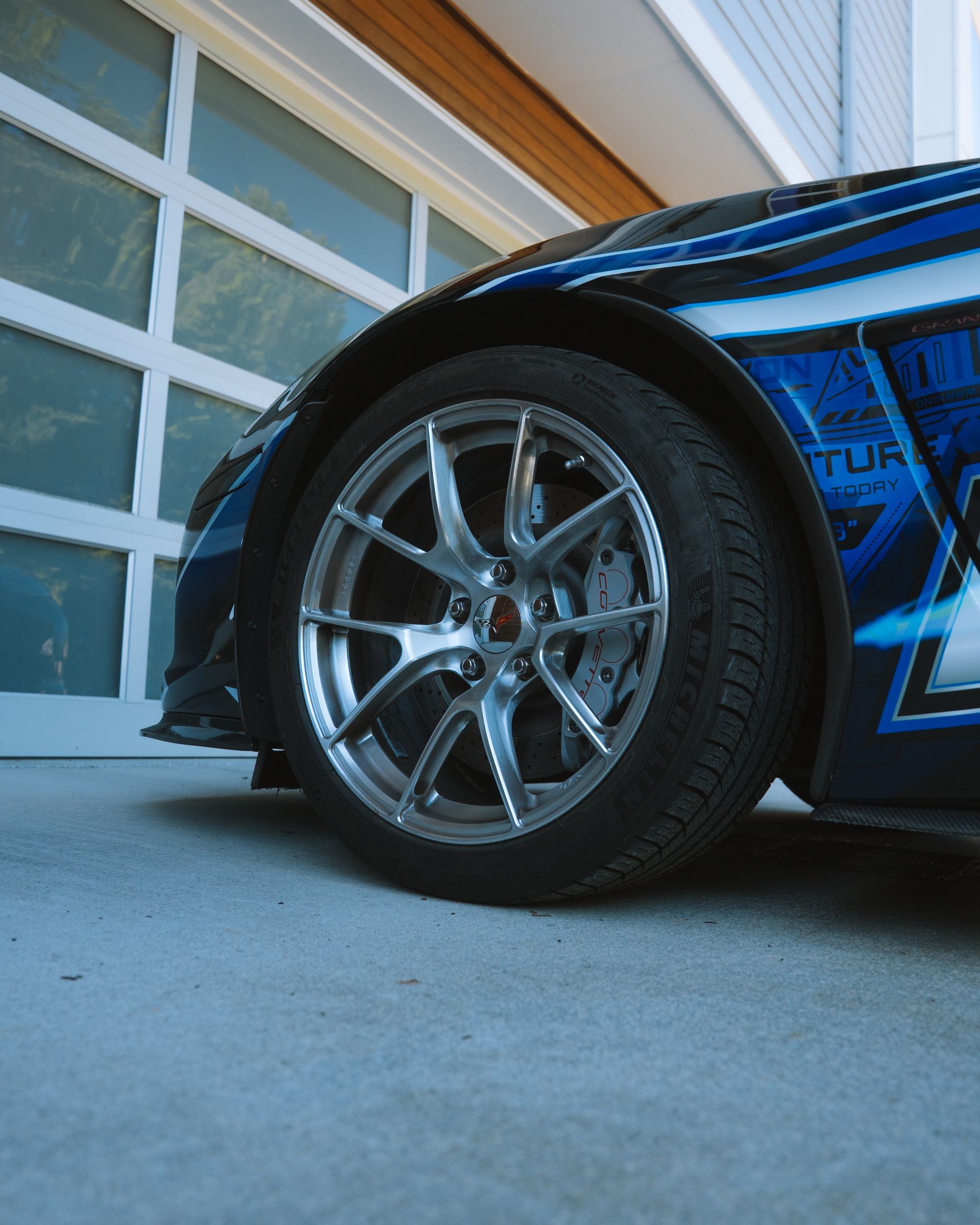Close-up of a blue race car’s front wheel parked beside a garage door