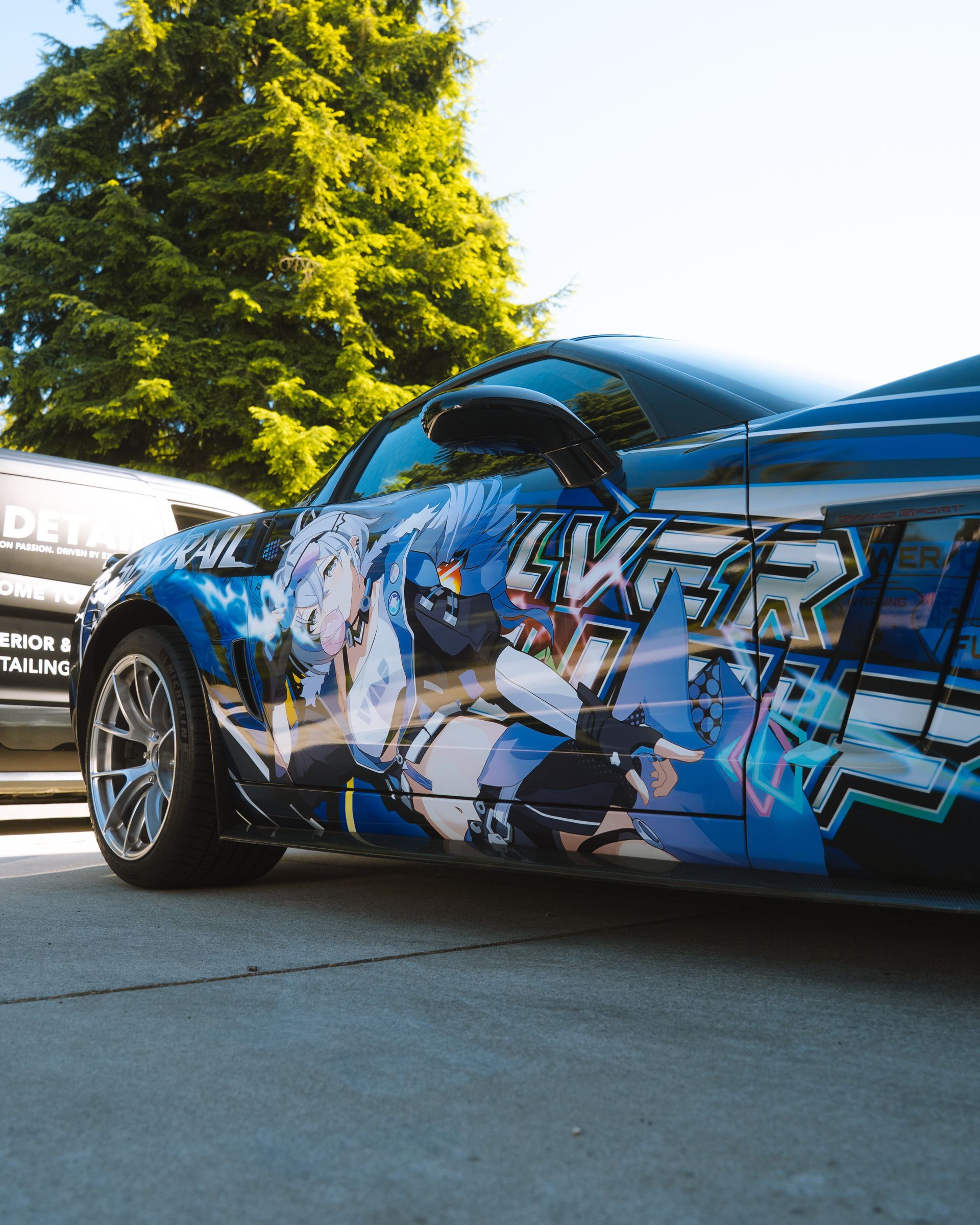Blue sports car with graffiti-style wrap parked outdoors in sunlight