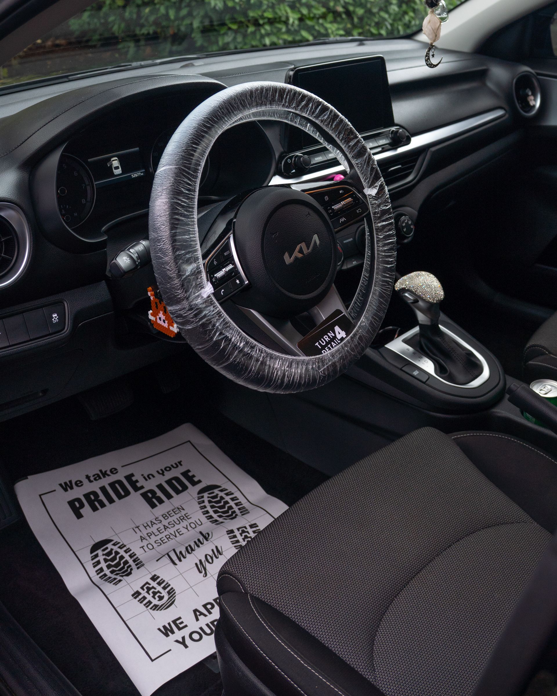 Car interior with steering wheel, dashboard, center console, and floor mat labeled “Pride in Ride”