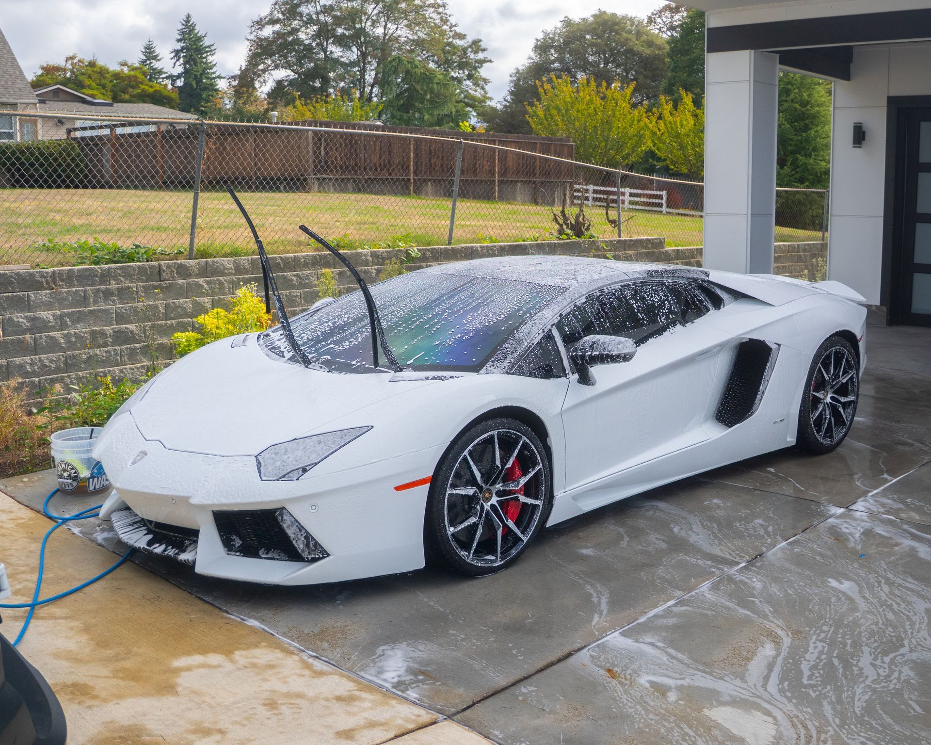 White sports car being washed in a driveway with a hose spray.