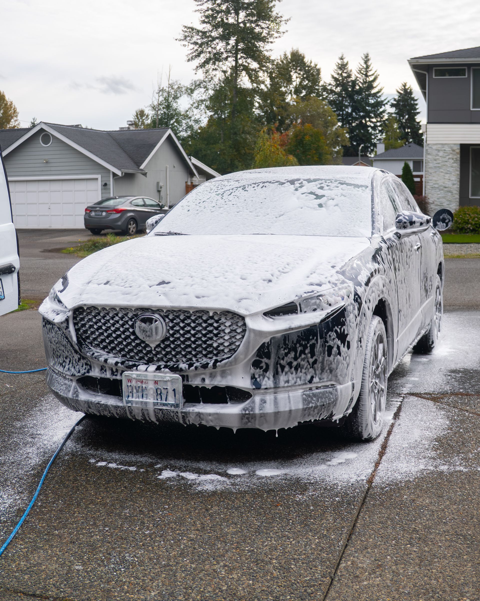 Car covered in foam during a driveway wash in a suburban neighborhood