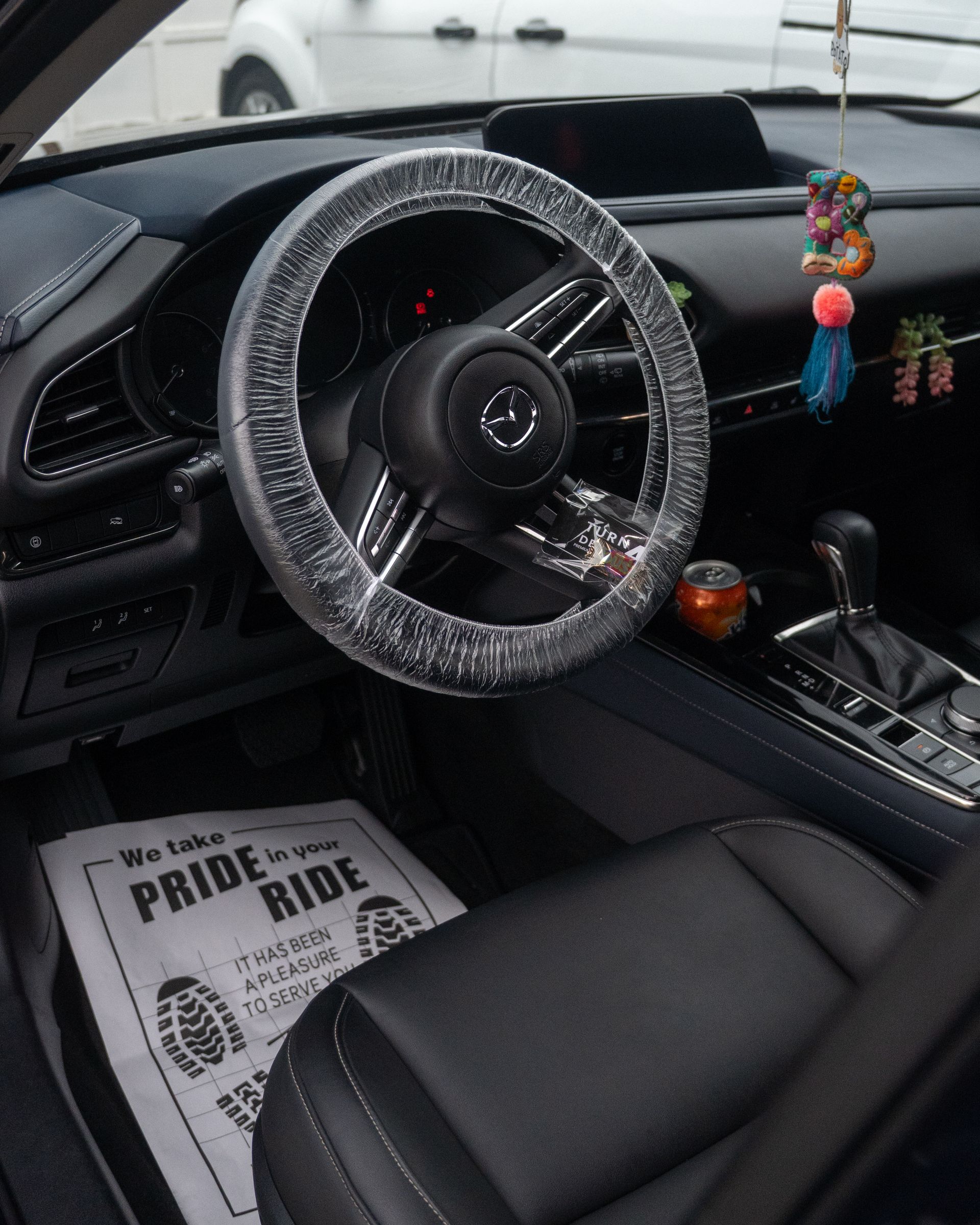 Car interior with a fur-covered steering wheel, hanging ornaments, and a Pride Ride floor mat