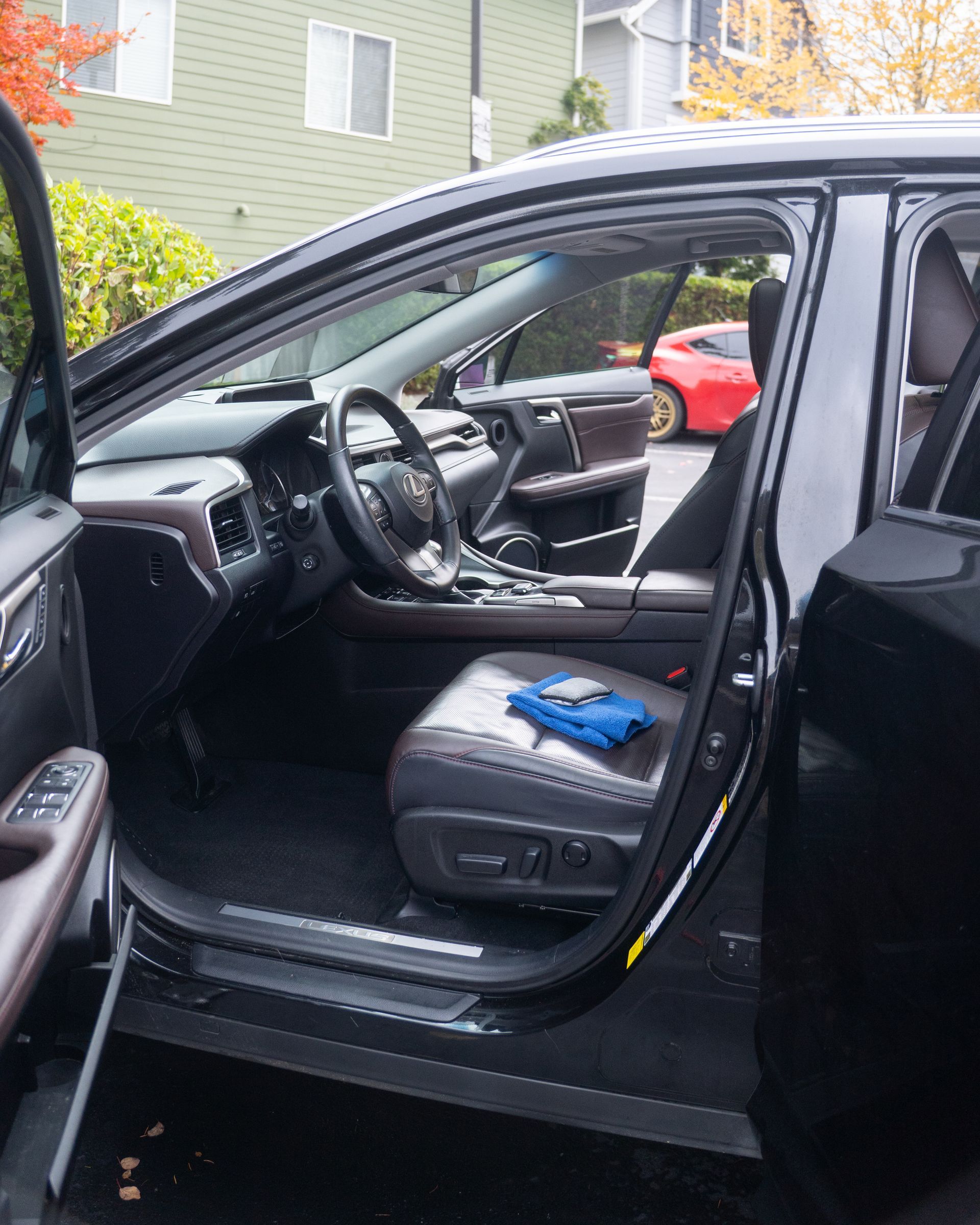 Open car door showing black interior with a blue item on the front seat, parked in a residential area.