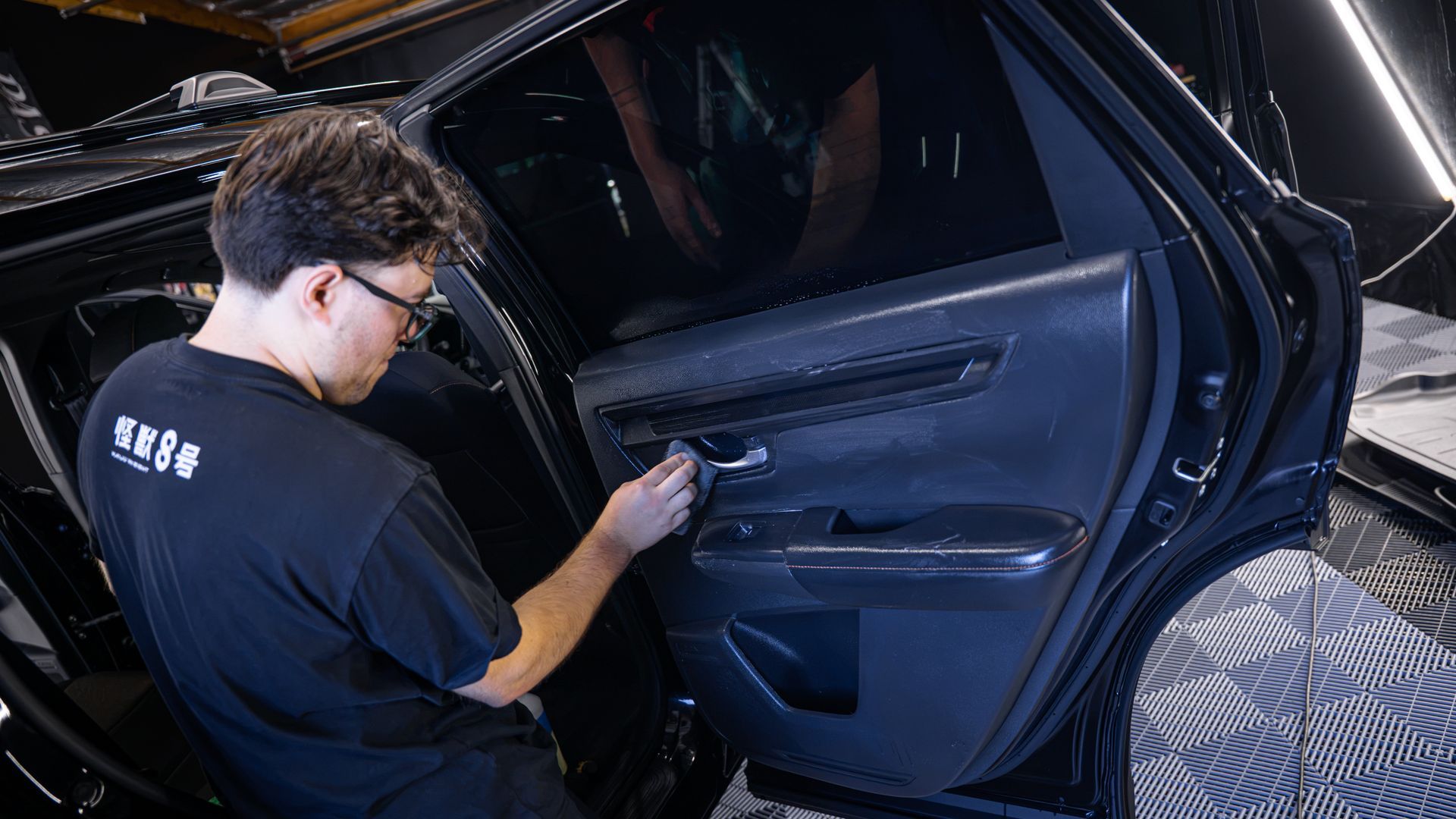 Technician applying tint or wrap to a black car door panel indoors