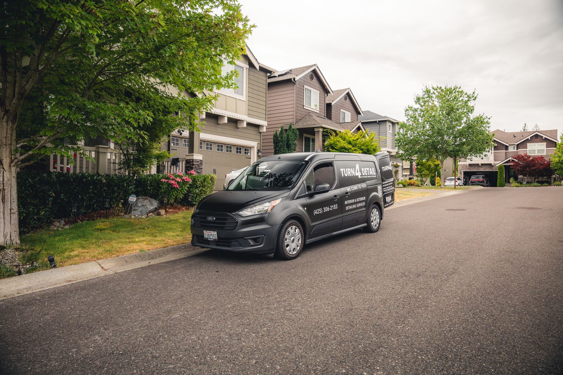 Black van parked on a quiet suburban street lined with houses and trees