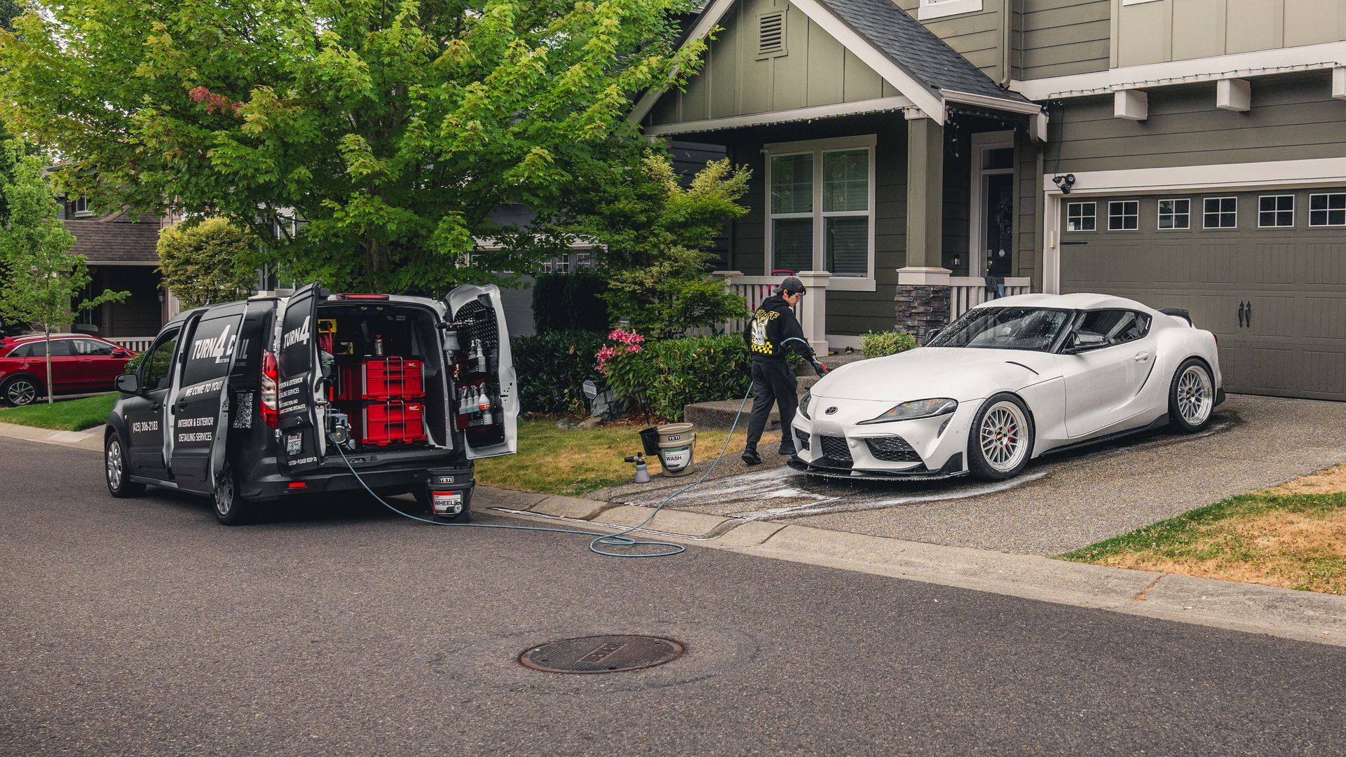Damaged white car and black van with open rear doors on a residential driveway beside a house