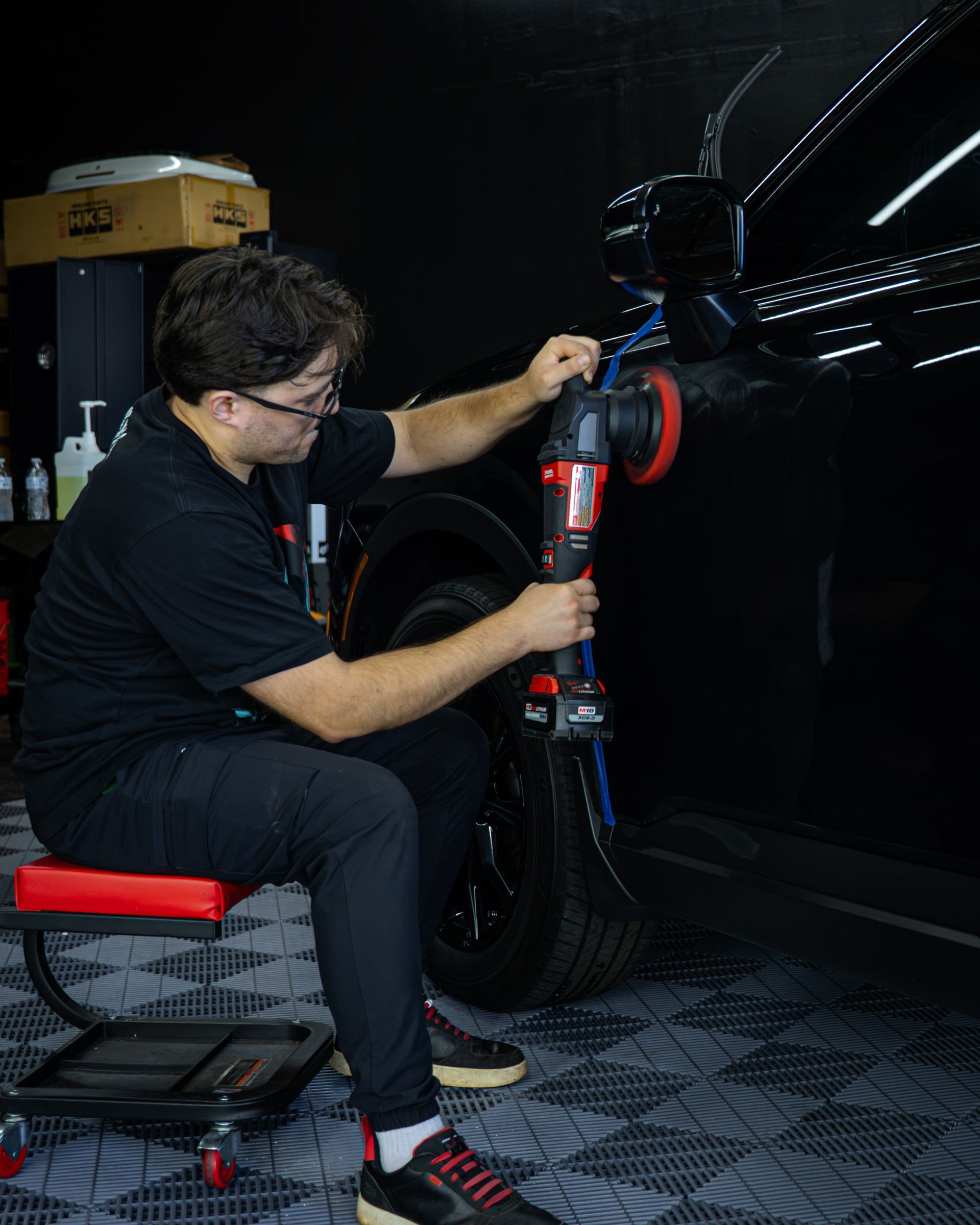 Mechanic adjusting a bicycle wheel in a dark workshop, seated on a red stool.