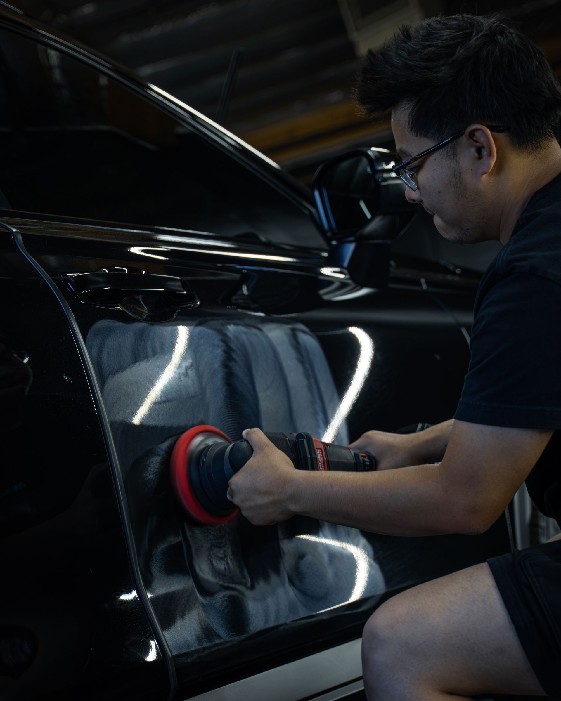 Person polishing a black car door with a buffer in a garage