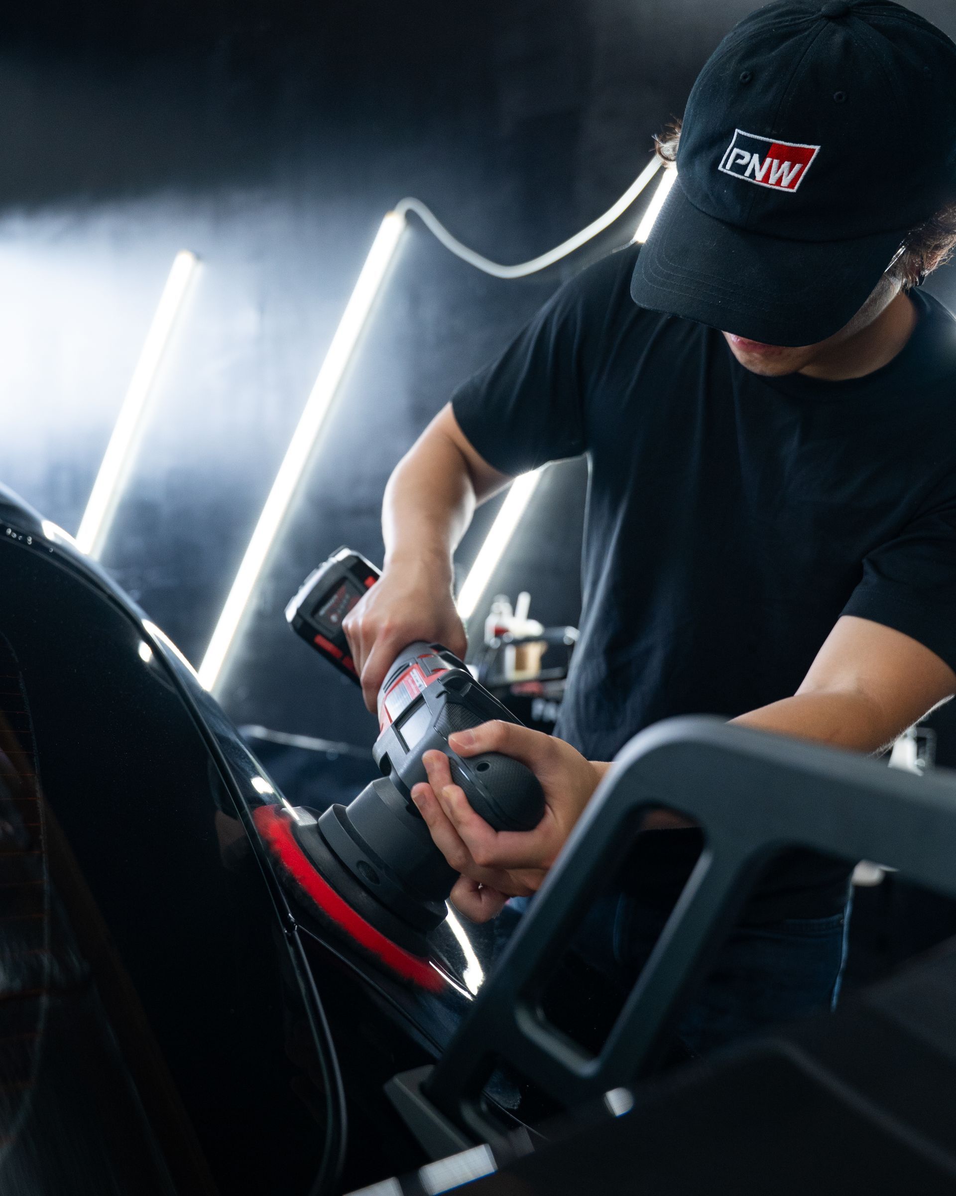 Mechanic using a power tool on a car in a dim garage, with bright light behind them