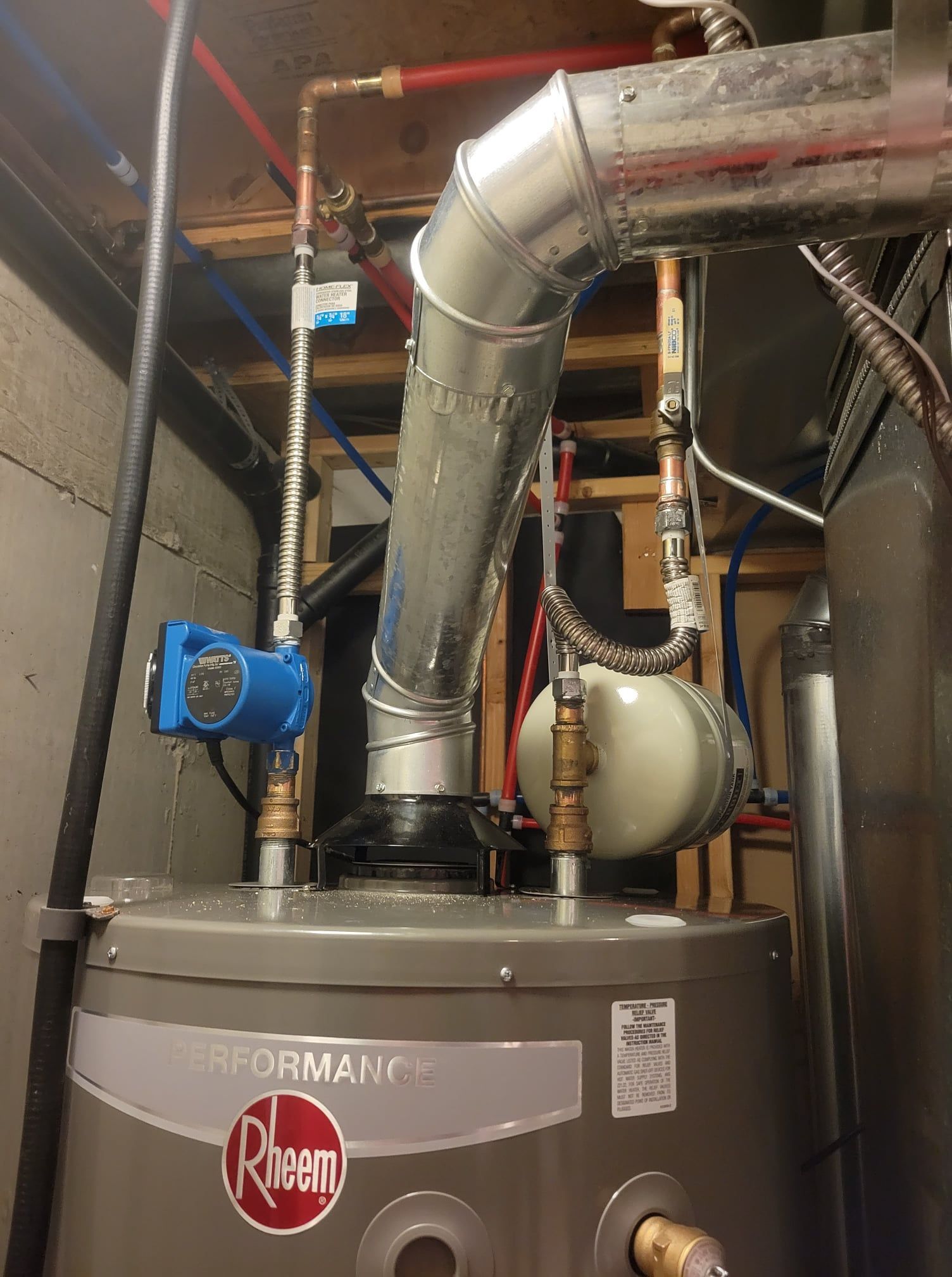 A rheem water heater is sitting in a basement next to a pipe.
