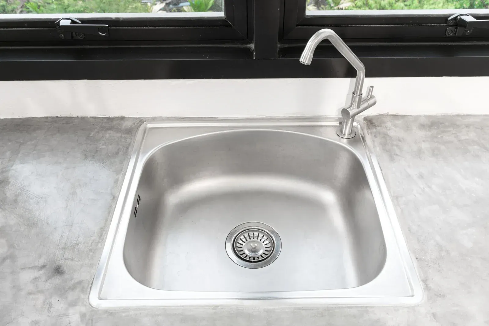 Stainless steel kitchen sink with faucet, set in a gray countertop, window in the background.