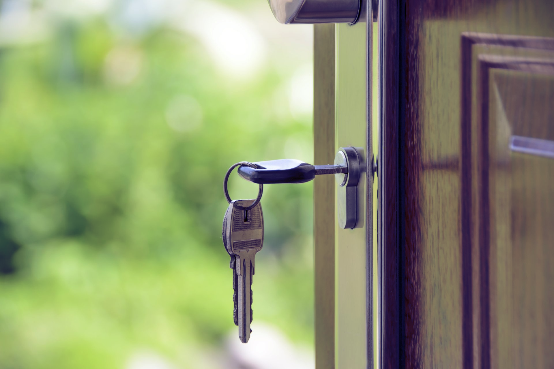 Keys in a door lock, partially open, with a green, blurred background.