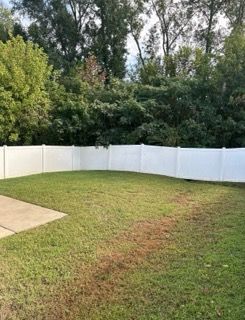 Backyard with green lawn, white vinyl fence, and trees in the background