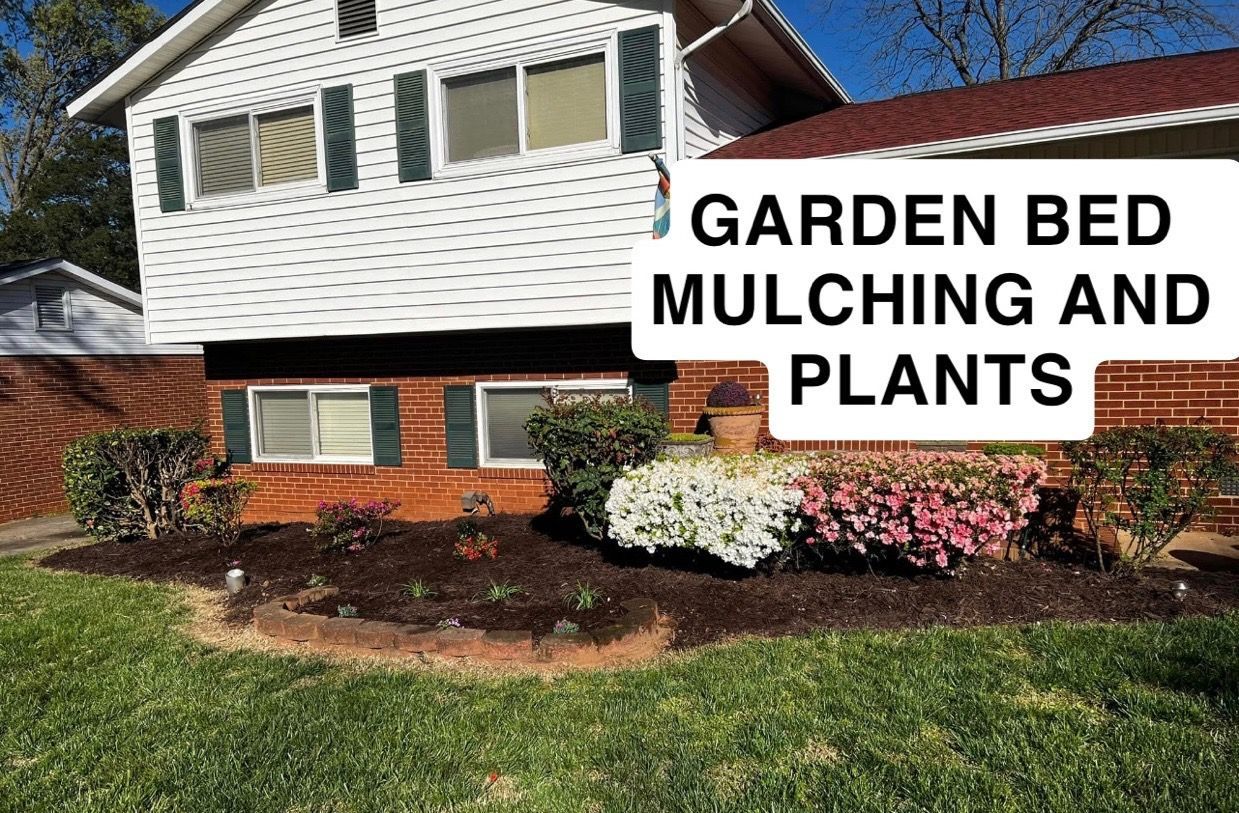 Front yard garden bed with mulch and blooming plants beside a house, labeled “GARDEN BED MULCHING AND PLANTS”