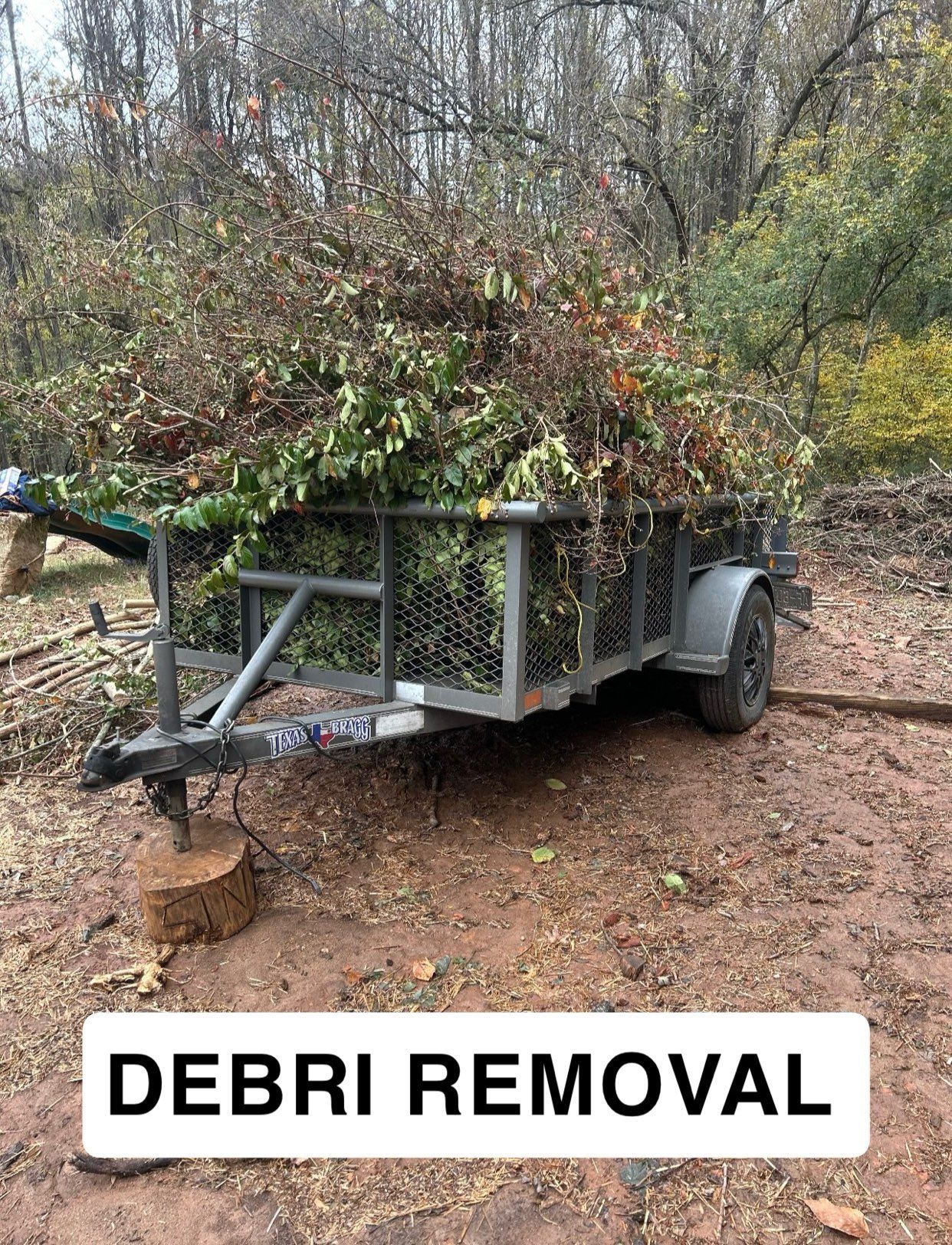 Trailer loaded with brush and branches in a wooded area, labeled “DEBRI REMOVAL”