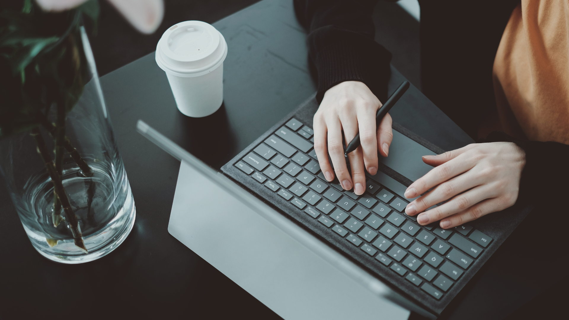 Hands typing on a laptop at a table with a coffee cup and water glass nearby.