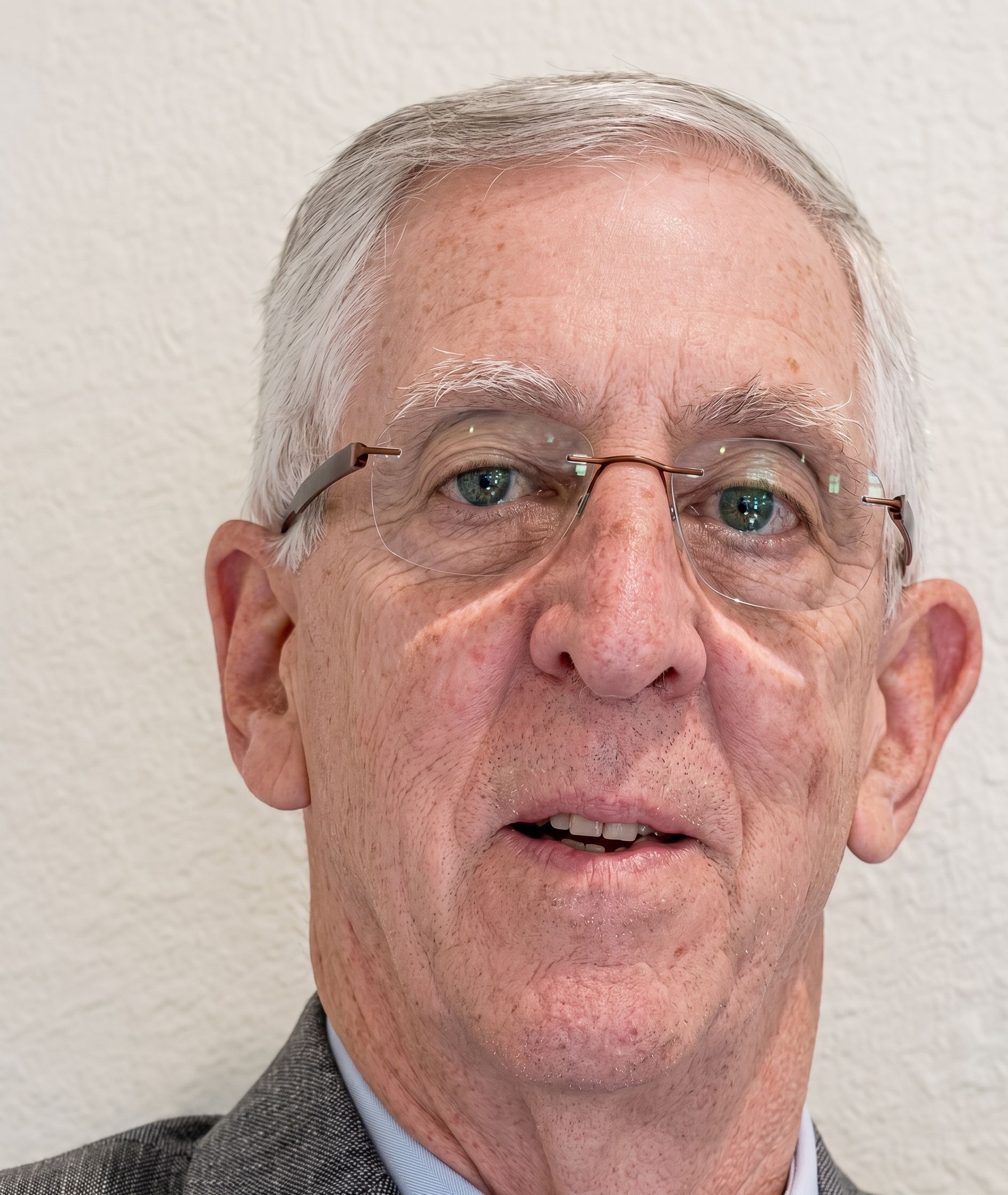 Portrait of a man wearing glasses and a gray blazer against a light background