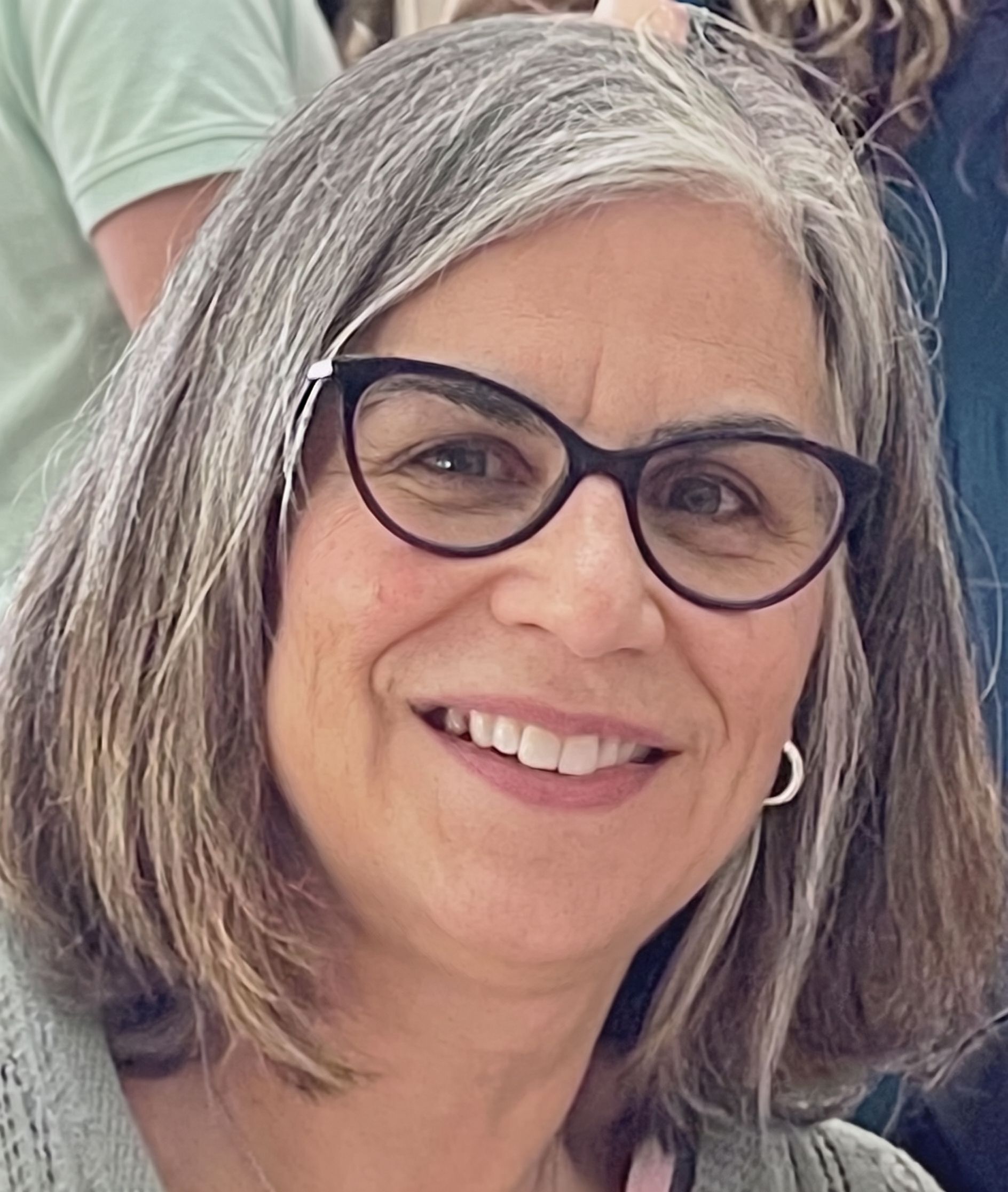Smiling person with gray hair and black glasses, in a close-up portrait.