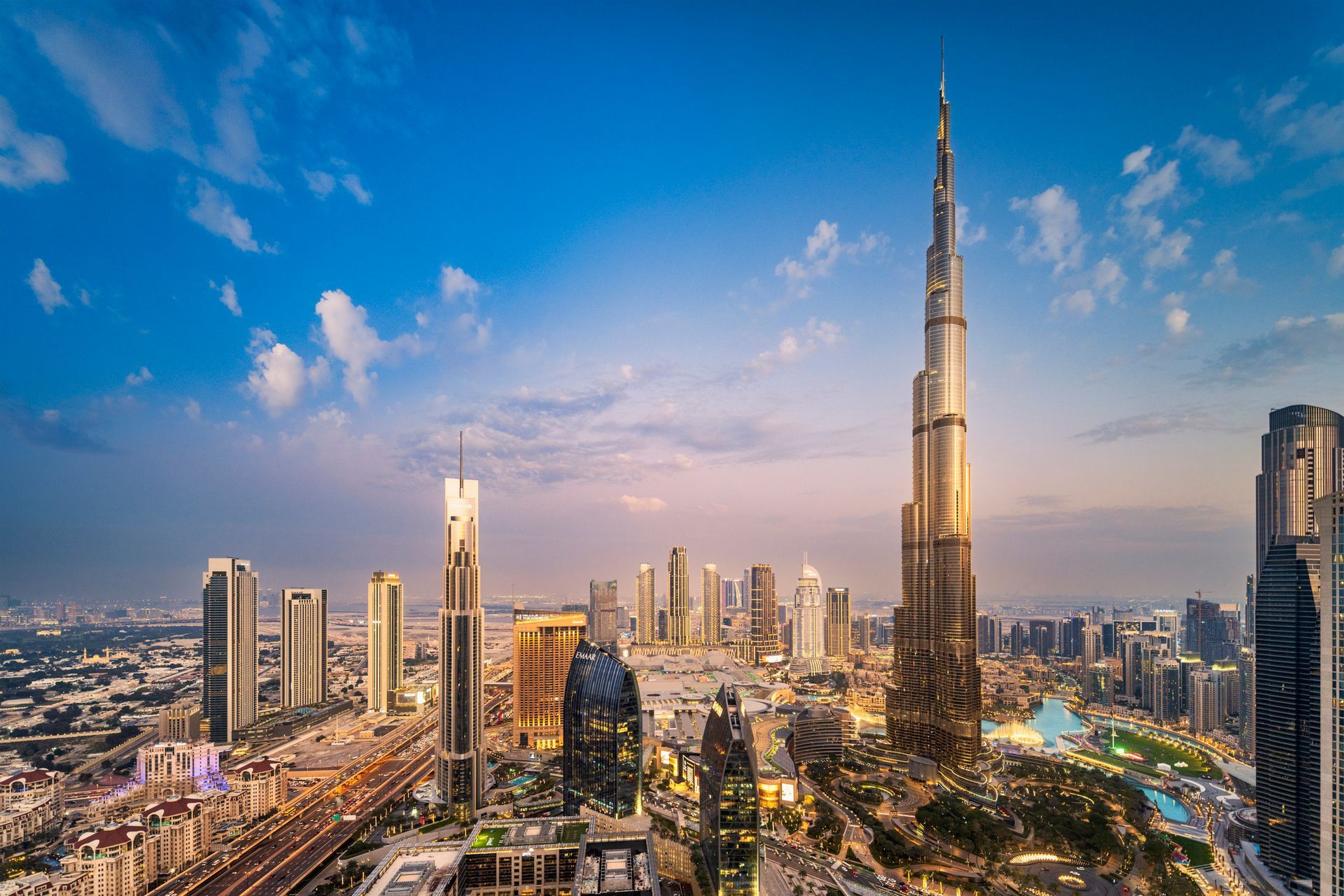 City skyline with the Burj Khalifa towering over other skyscrapers under a blue sky.