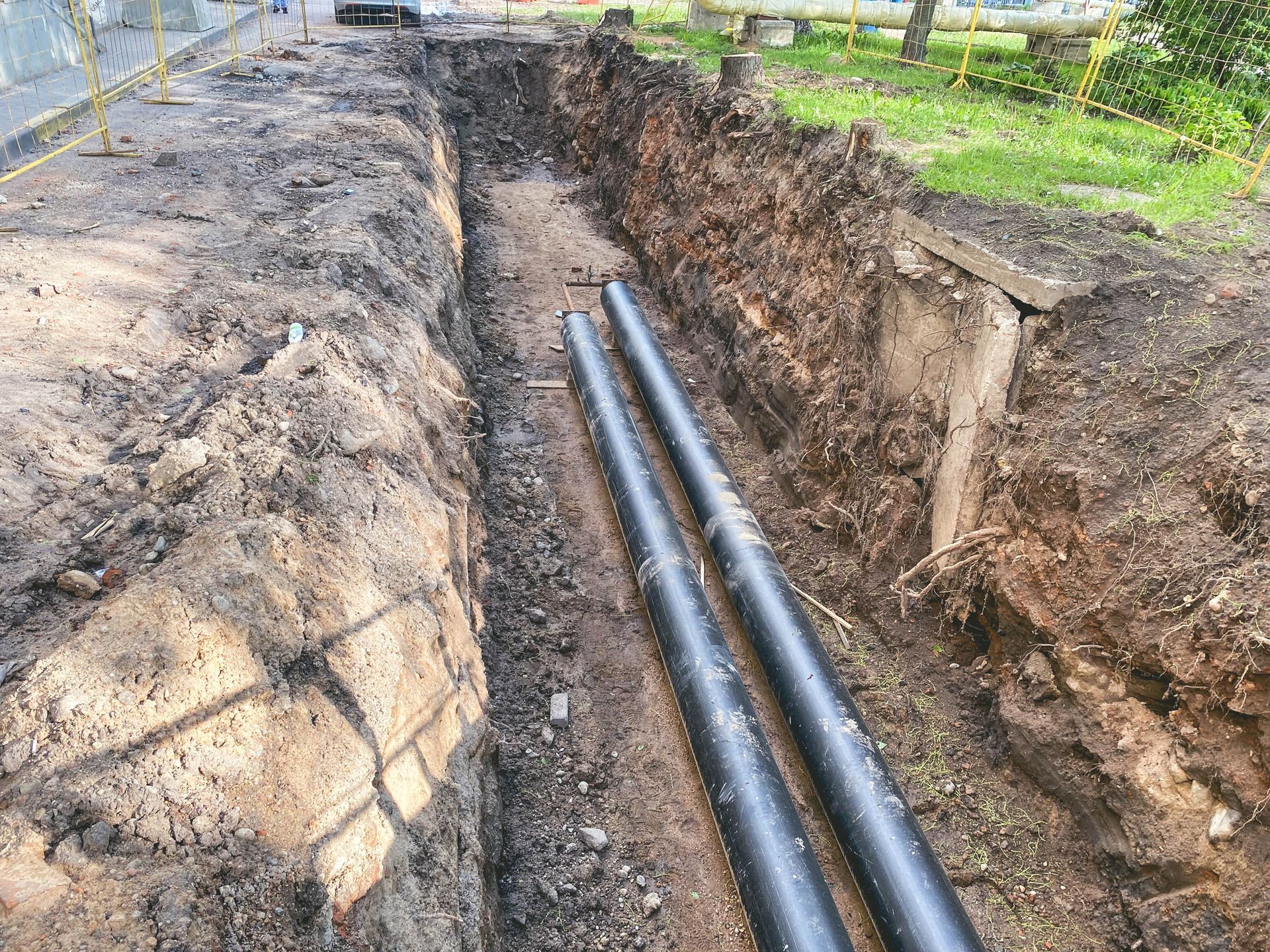 A long, narrow trench in the ground containing two parallel black pipes, with dirt walls on either side.
