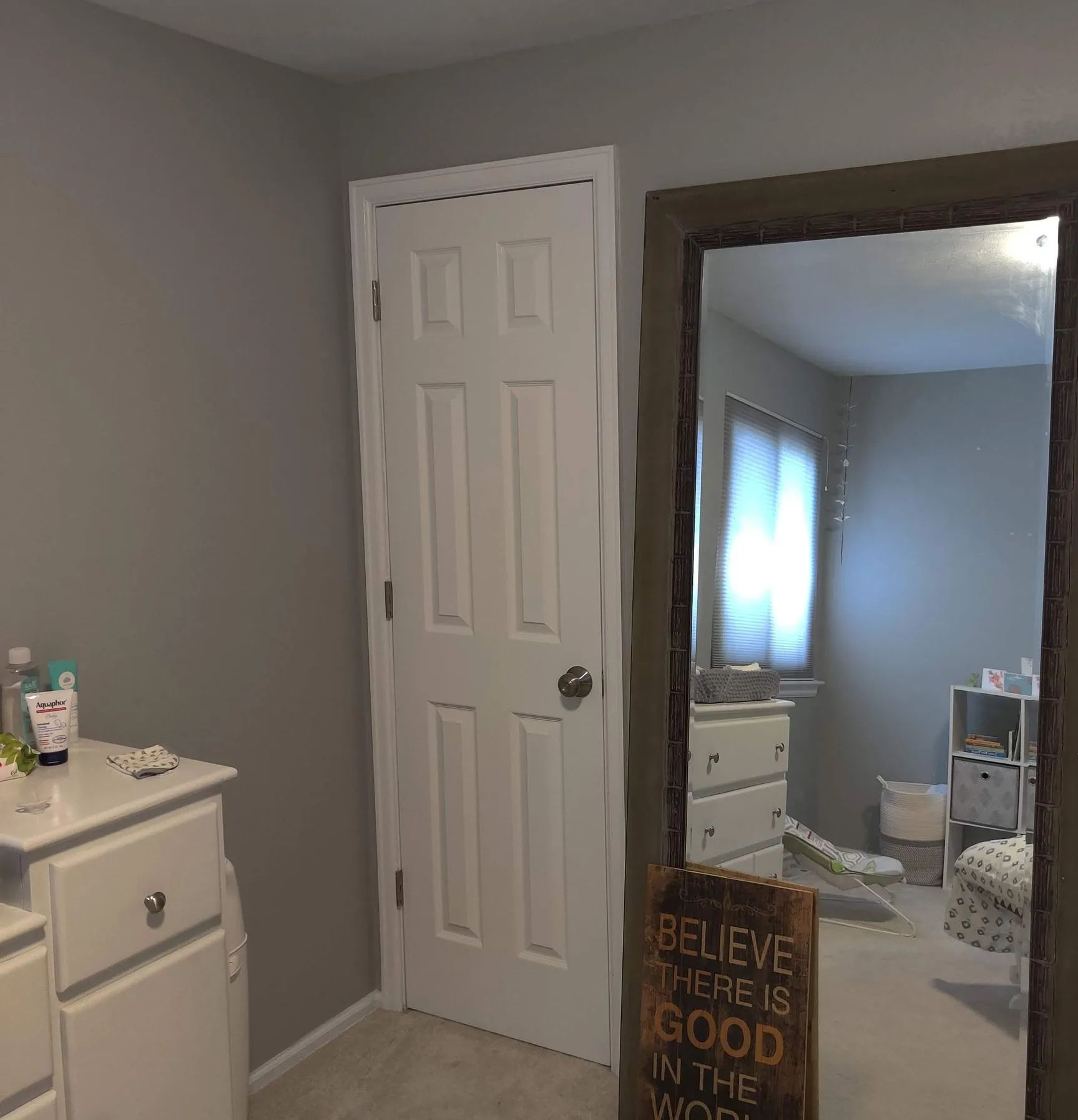 Bedroom with gray walls, white closet door, mirror, and dresser reflecting a window-lit room.