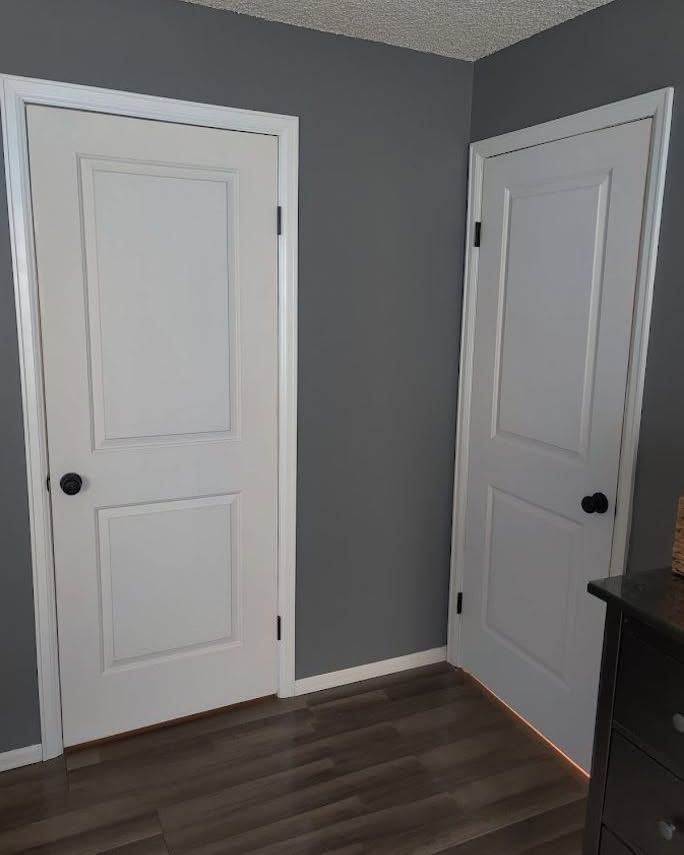 Corner of a room with gray walls, dark wood floor, and two white interior doors.