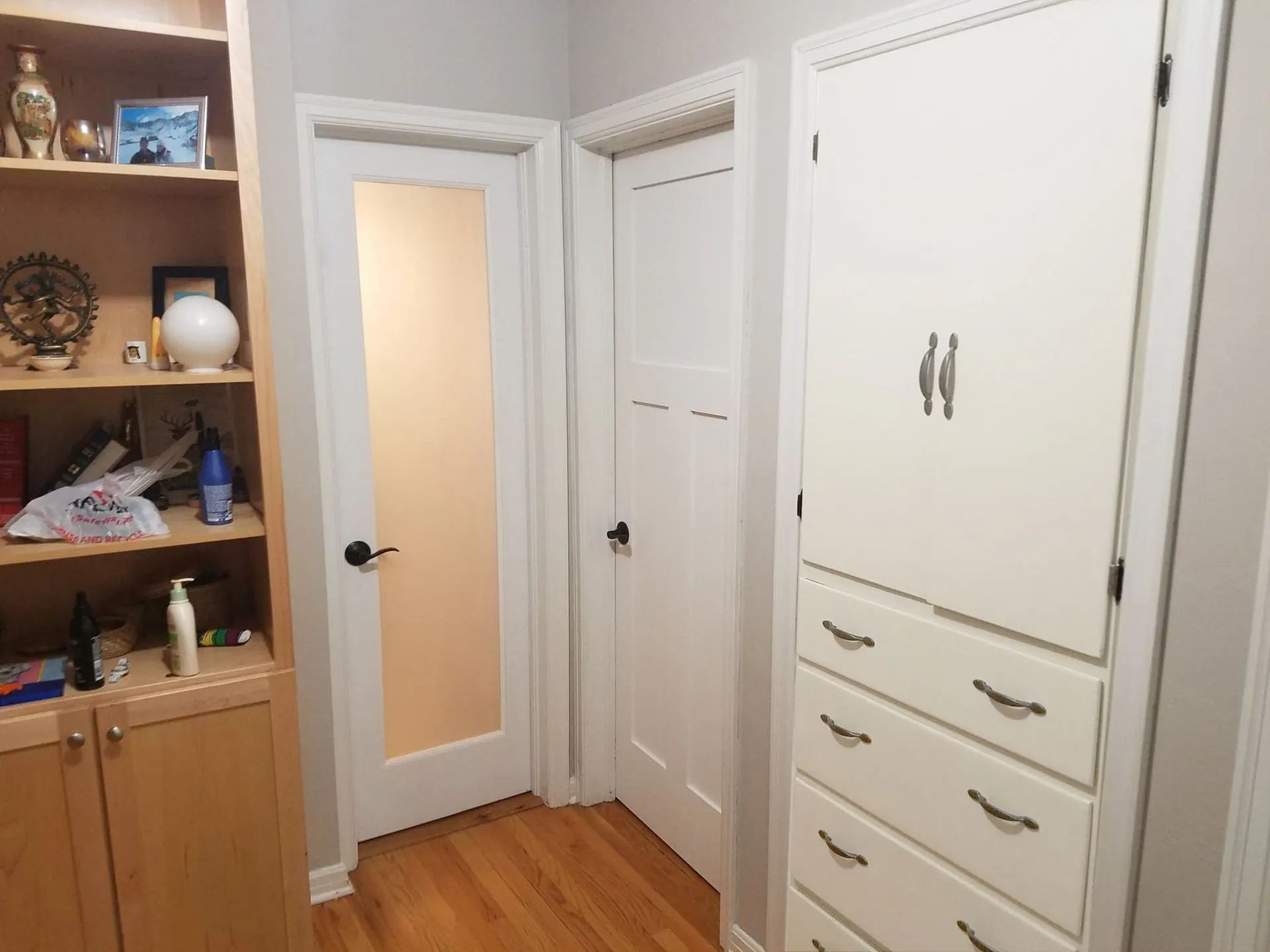 A hallway with a built-in cabinet, a frosted glass door, and wooden floors.