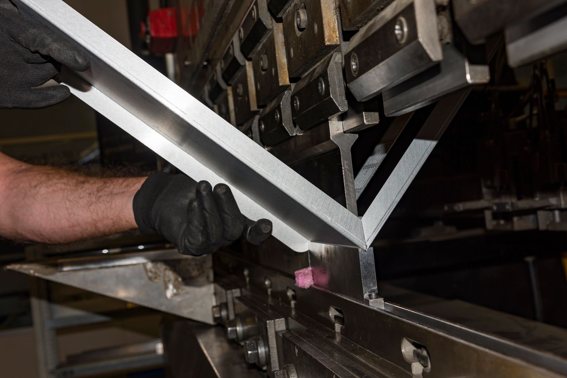 Una mano guantata guida una barra di metallo attraverso un macchinario industriale su una linea di produzione.