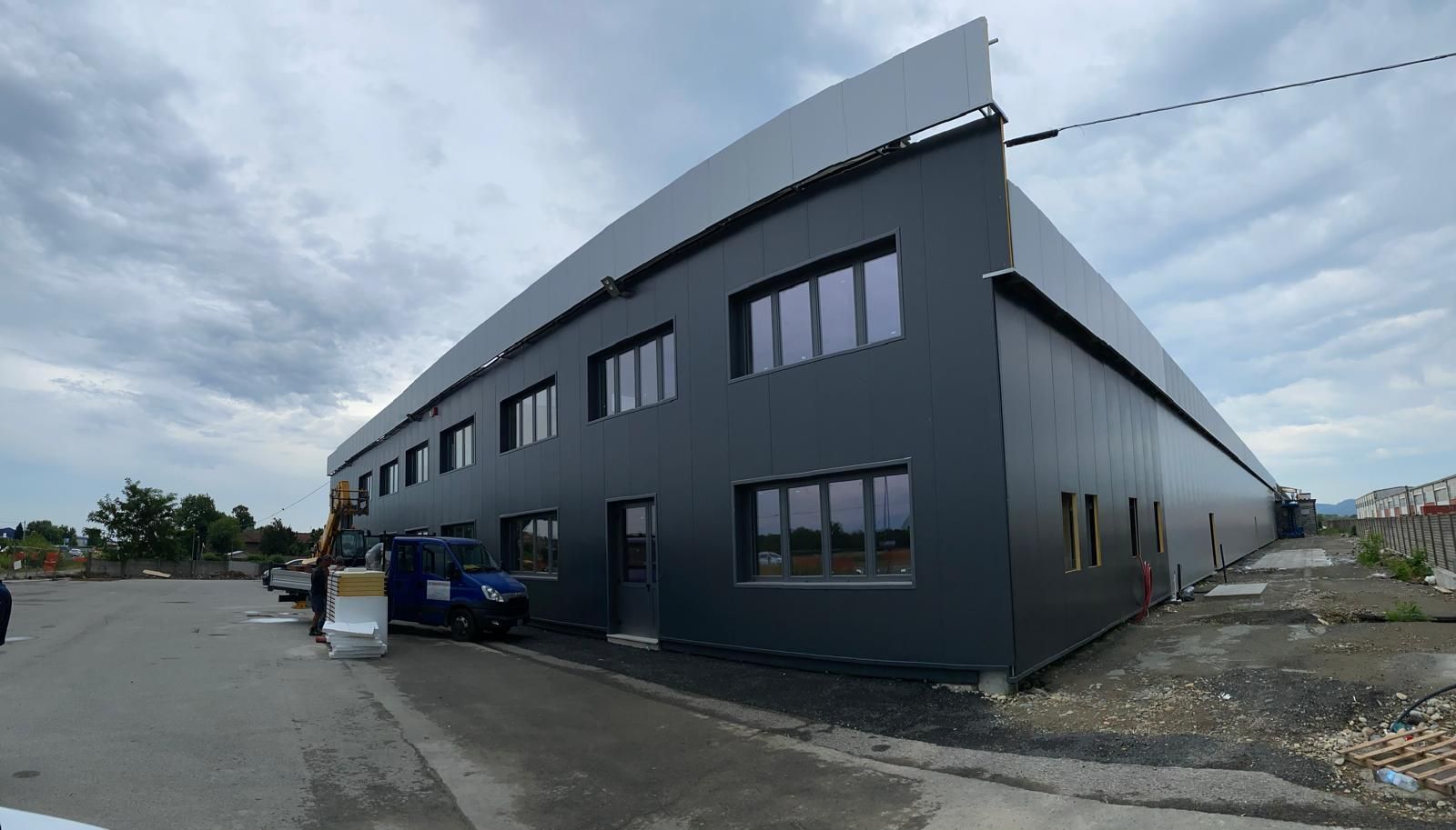 Edificio commerciale moderno di colore grigio scuro con tetto spiovente, su un lotto pavimentato sotto un cielo nuvoloso.